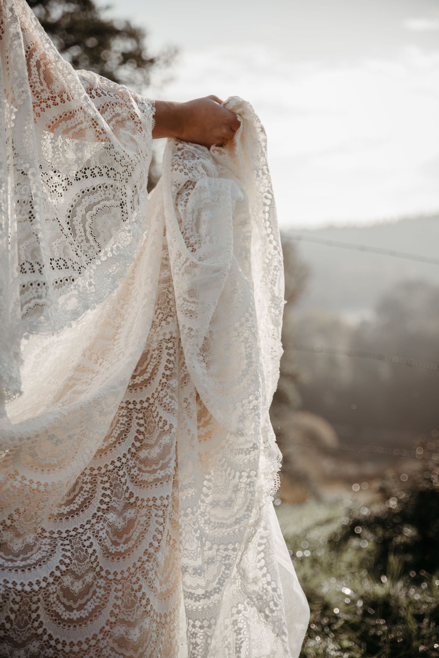 Sunlit lace wedding dress details show intricate patterns against a mountain vista.