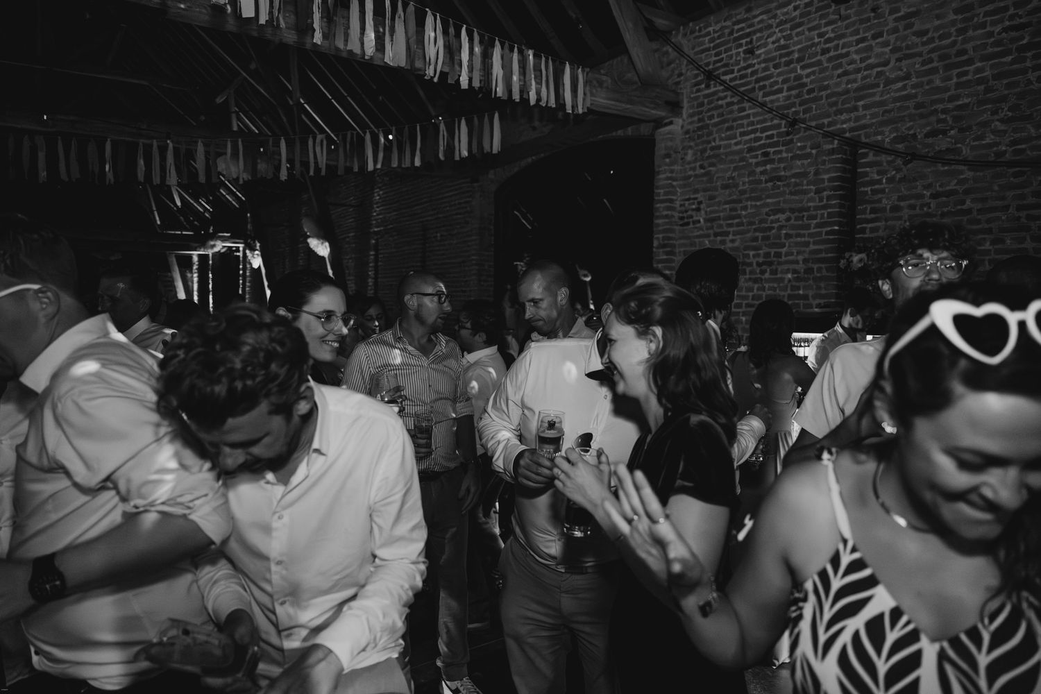 Black and white photo of people dancing at a lively wedding reception.