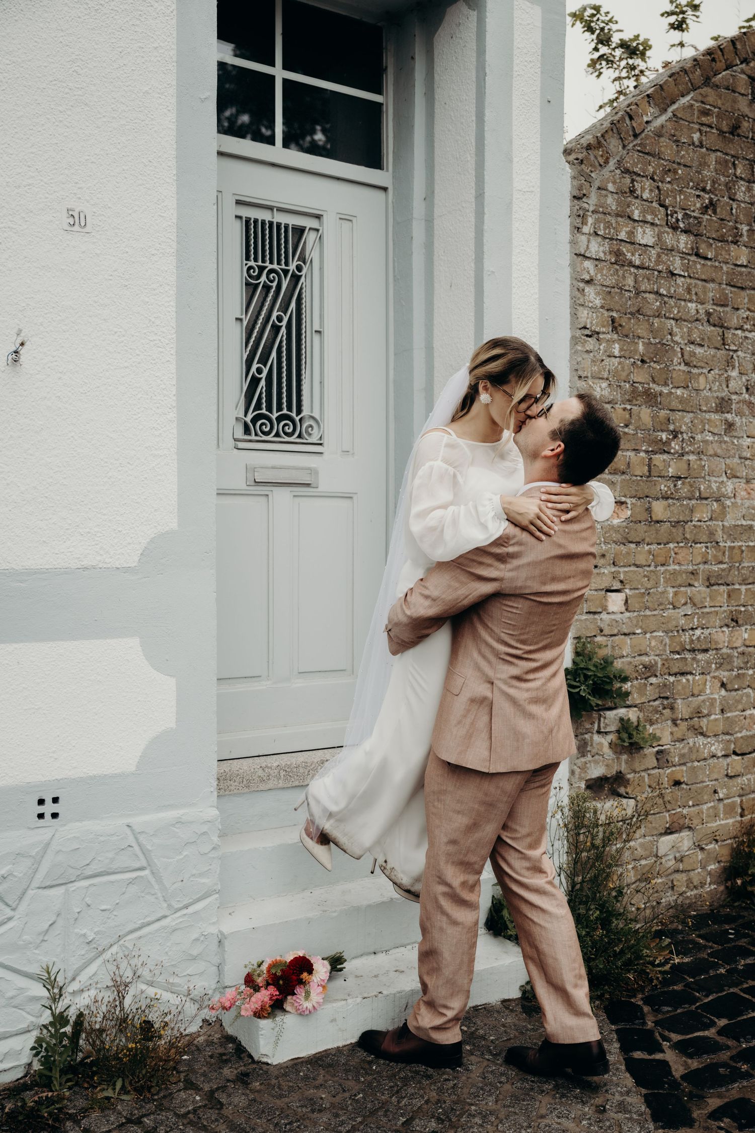 Couple embracing in front of a white building wearing matching beige and white outfits.