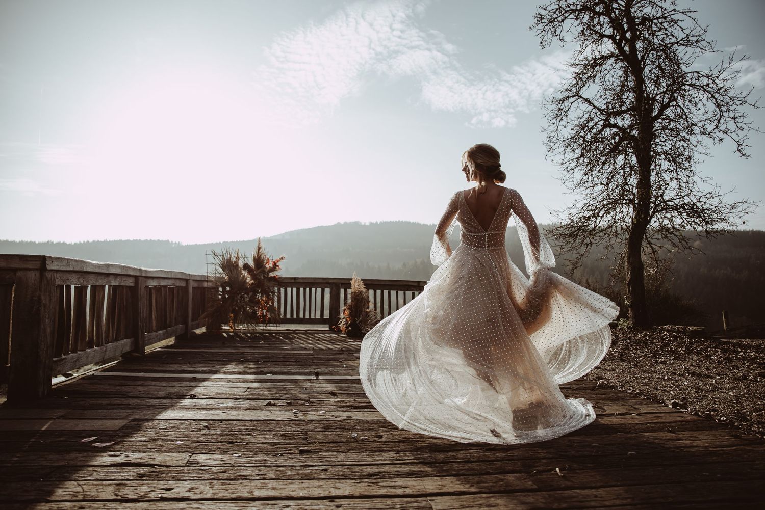 Bride spinning in flowing white dress on rustic deck with mountains in background.