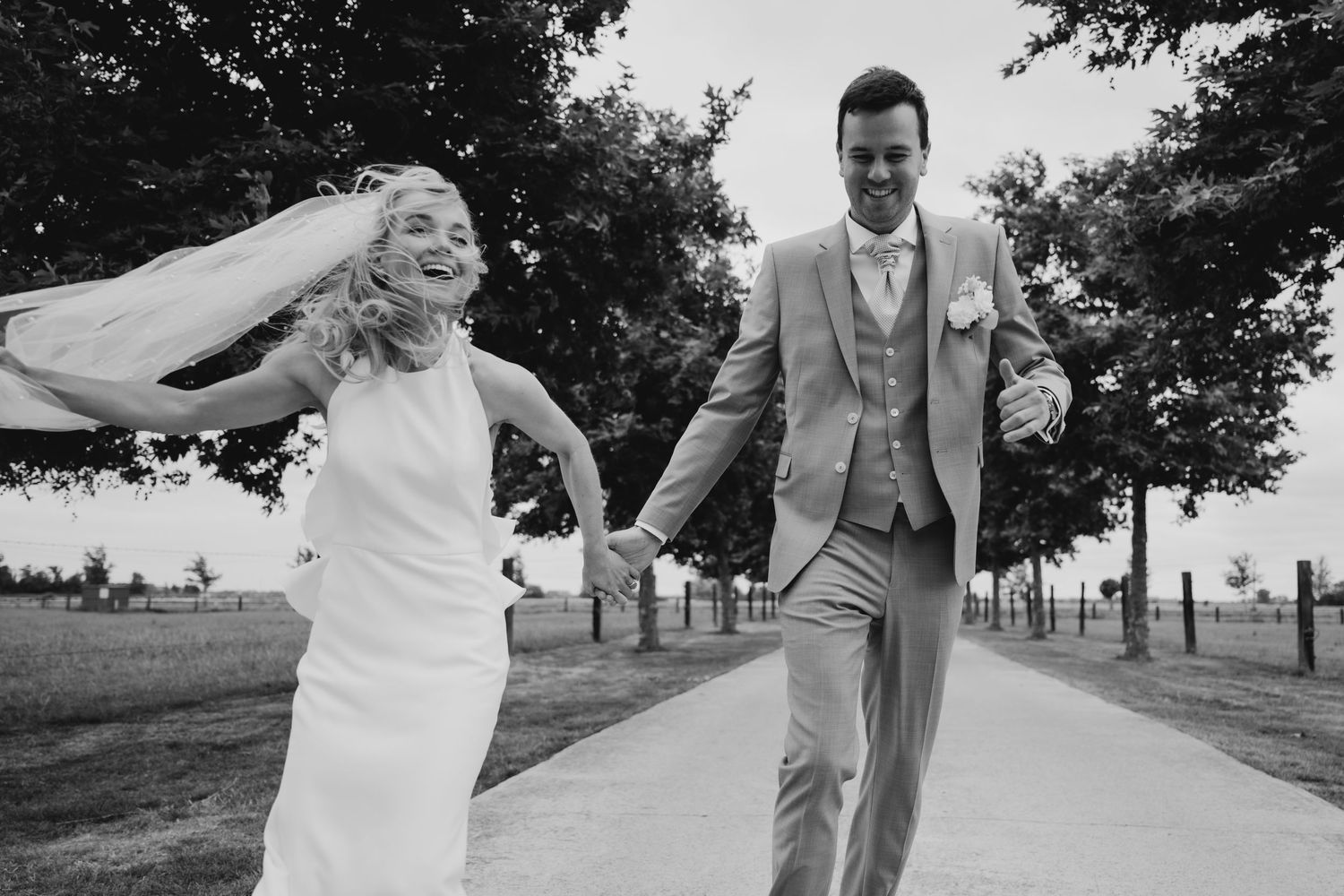 Wedding couple walking and posing along a tree-lined path in black and white.