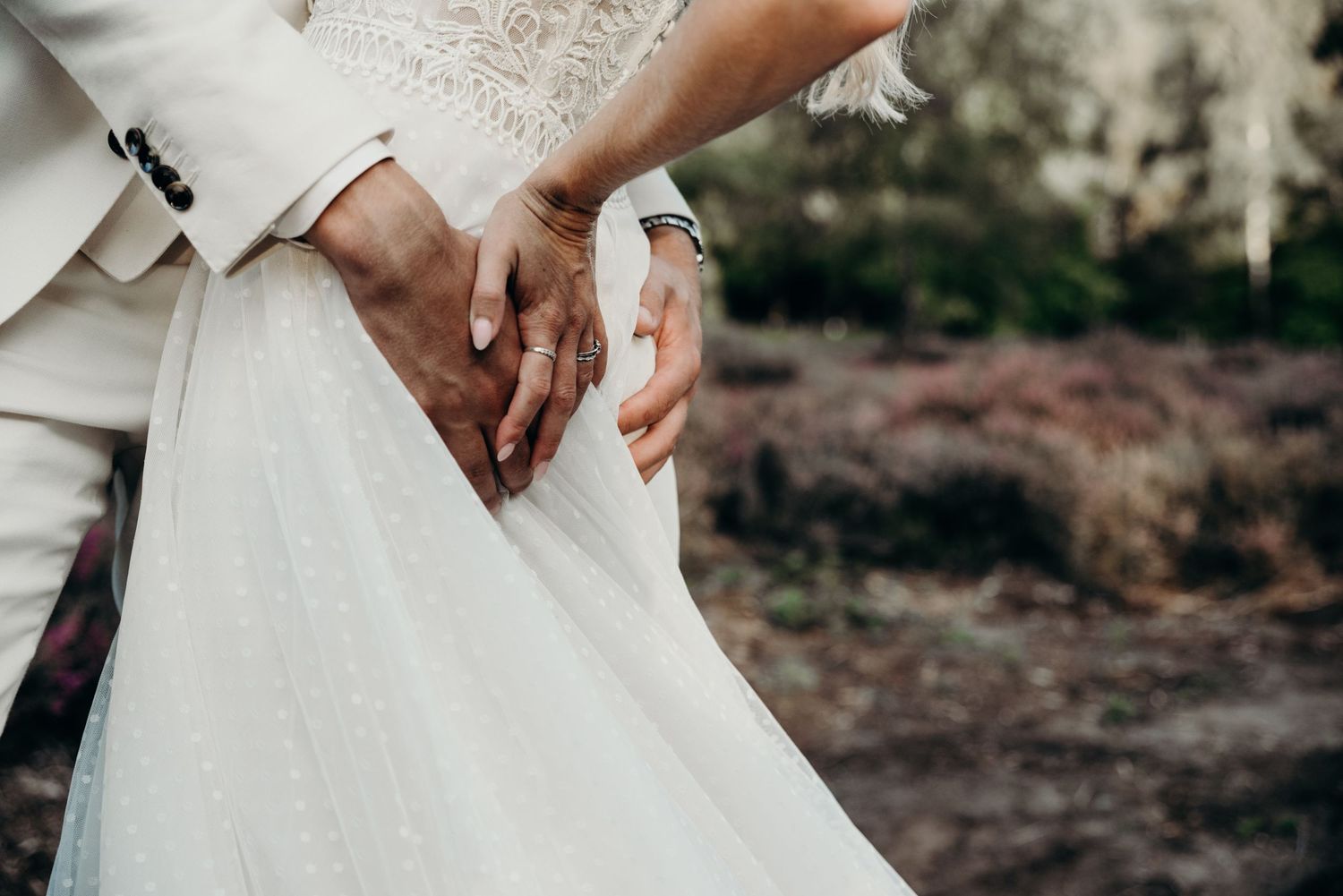 Close-up detail shot of hands holding wedding dress fabric against natural backdrop.