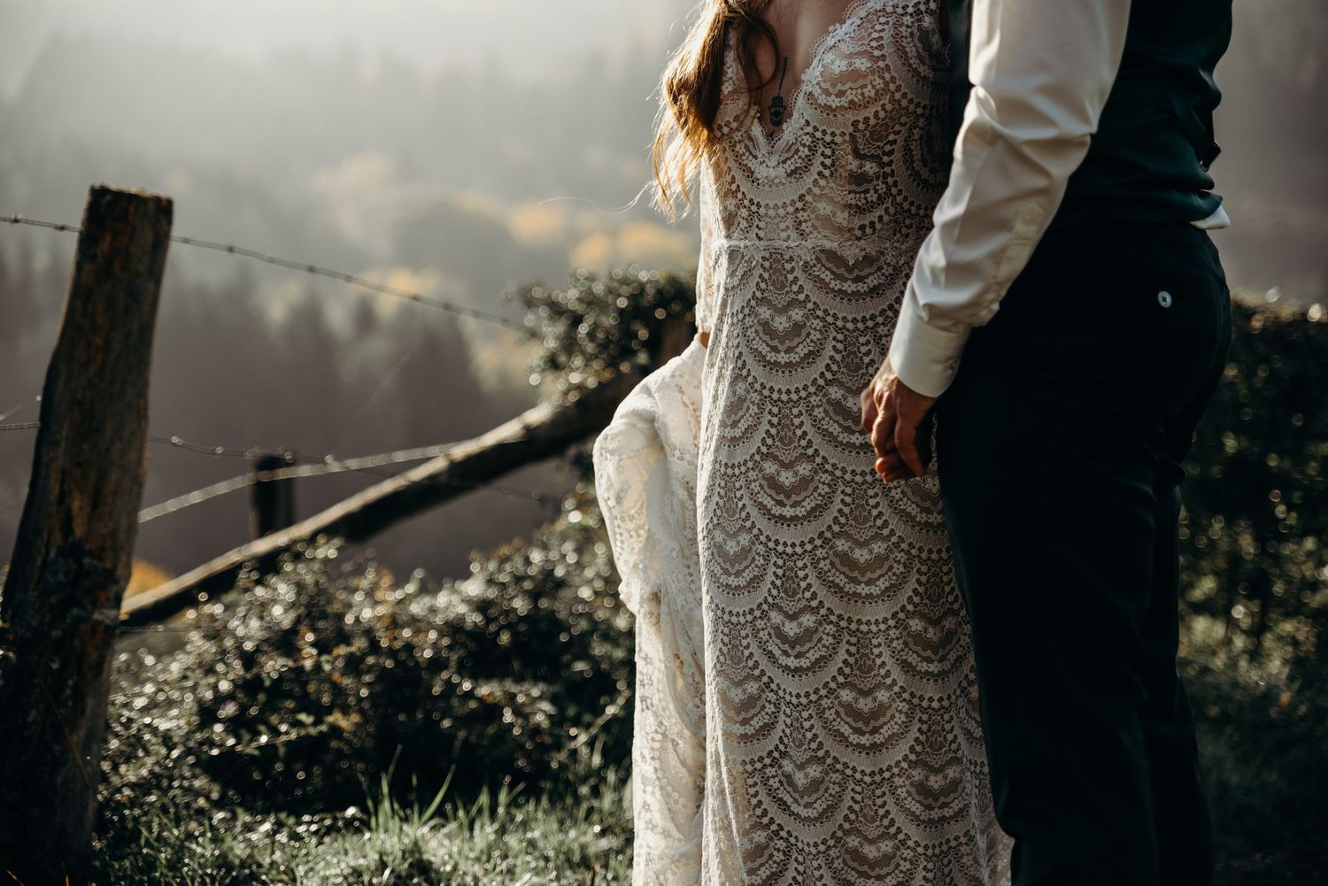 A lace wedding dress with intricate details flows in the outdoor breeze against a mountain backdrop.