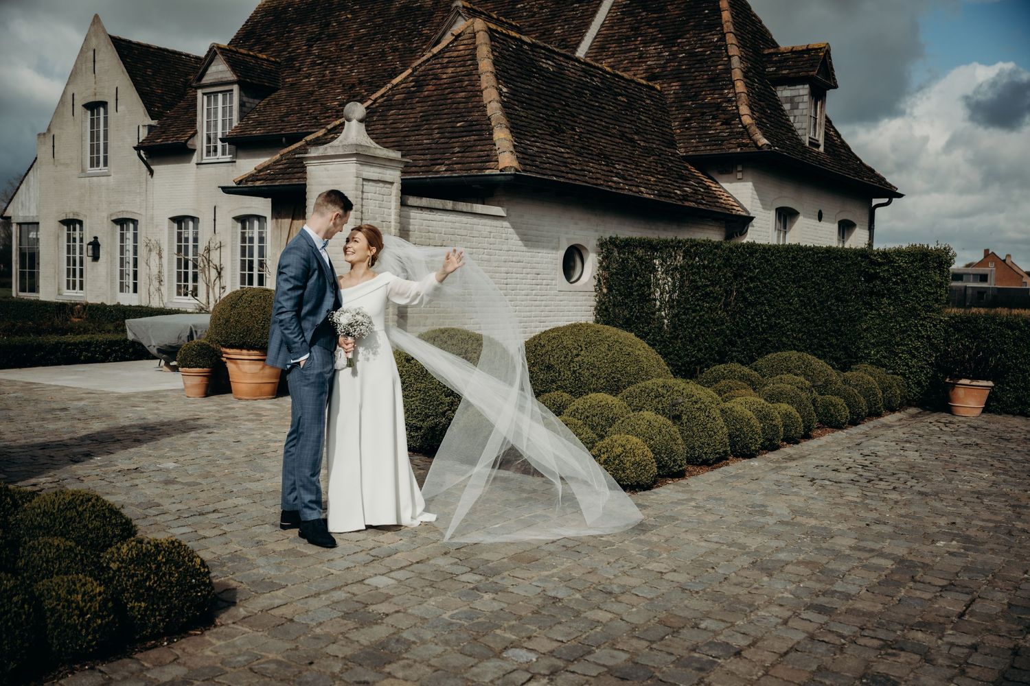 Elegant wedding venue with stone buildings and manicured hedges on a cloudy day.
