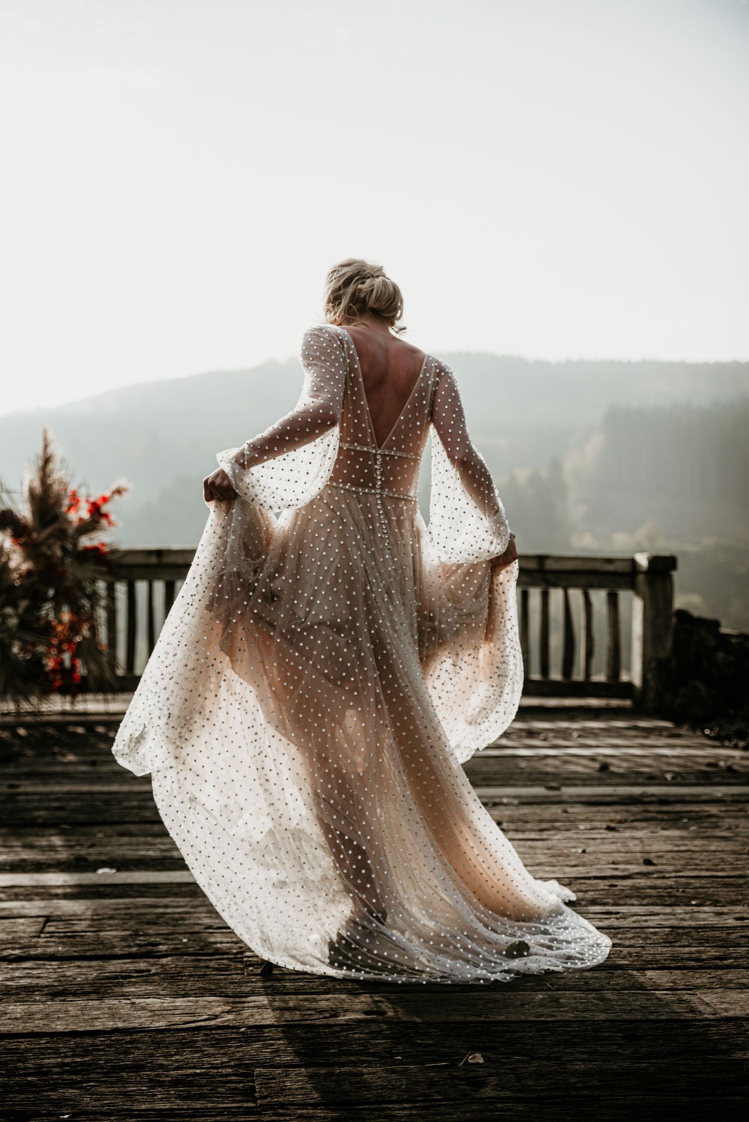 Bride in lace dress twirling on wooden deck with mountain vista backdrop.