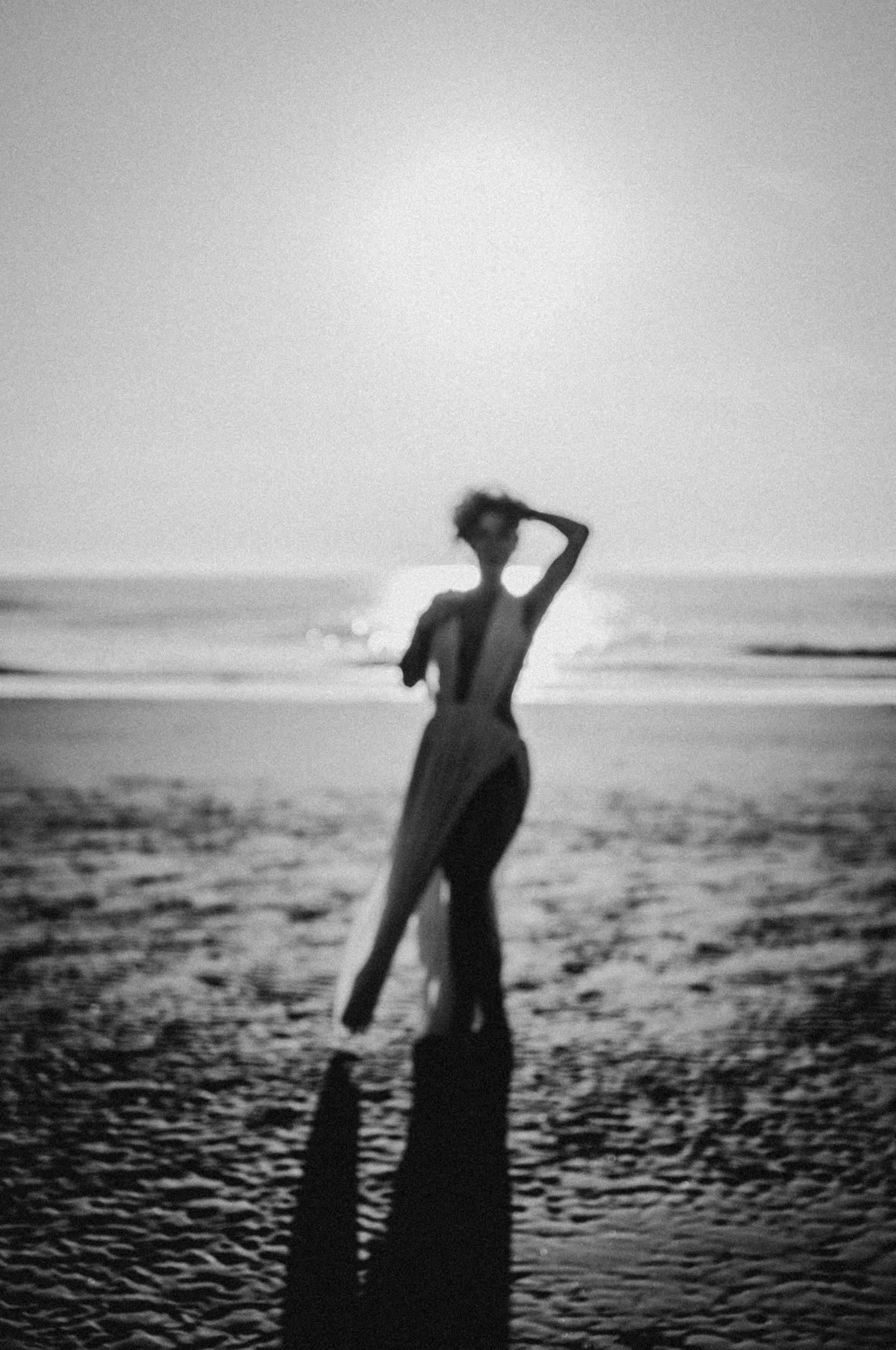 A series of black and white silhouettes on a beach show a figure in motion against a textured shoreline and sky.