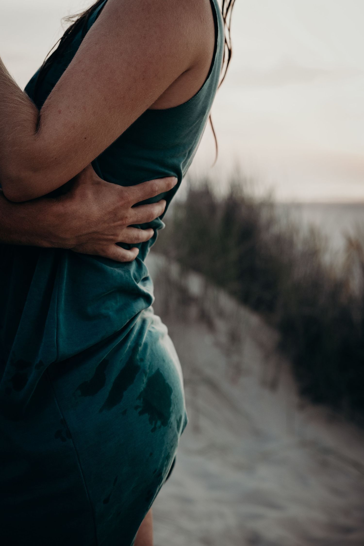 Close-up series of a pregnant woman's belly in a teal dress against a moody outdoor background at sunset.
