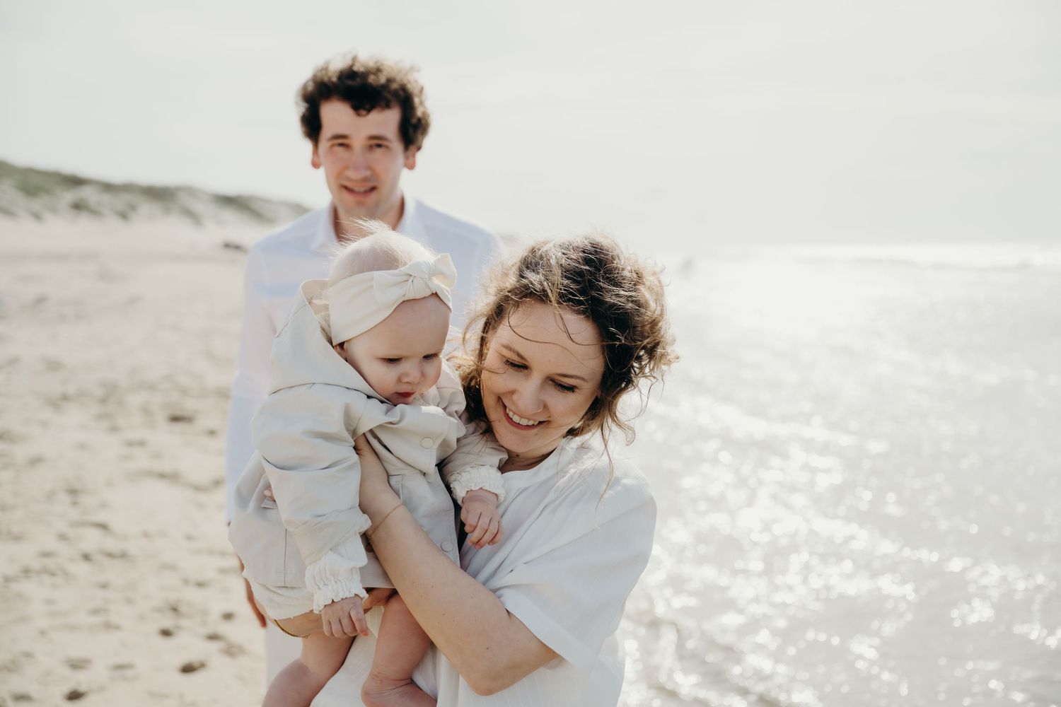 Family plays together on sunny beach with ocean waves in background.