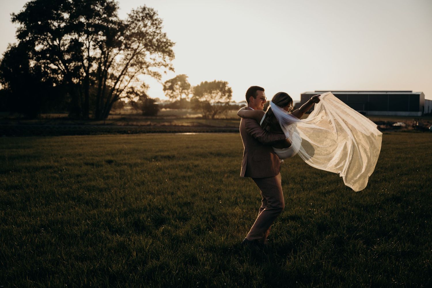 Silhouette of couple dancing in open field during sunset with flowing dress movement.