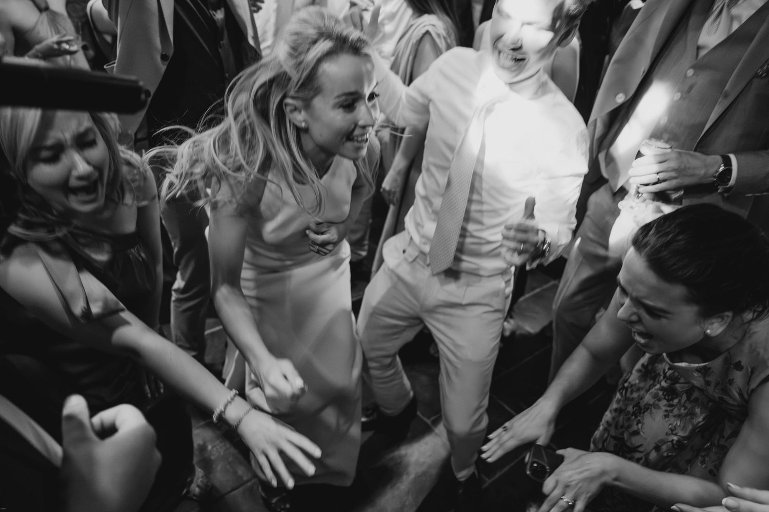 Black and white candid shots of wedding guests dancing and celebrating at a reception.