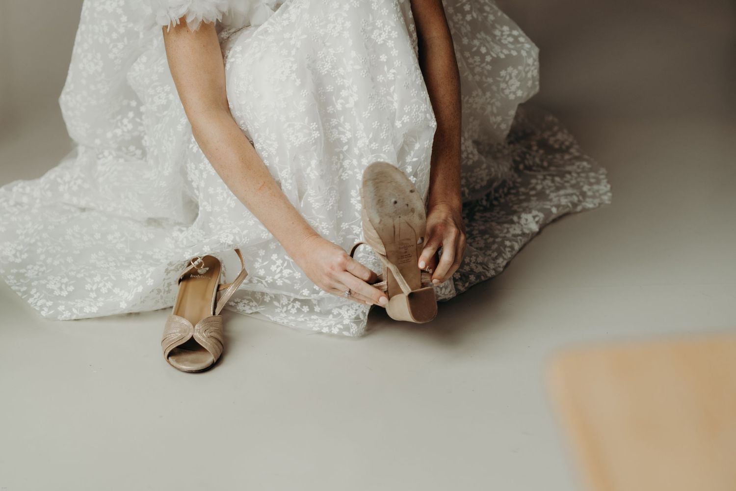 Close-up of hands adjusting beige wedding shoes with lace dress details.