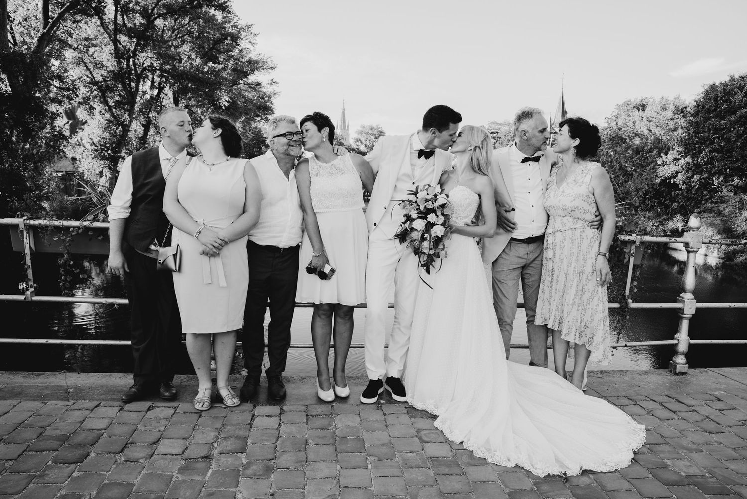 A wedding party poses together on a brick patio for a formal black and white group photo.