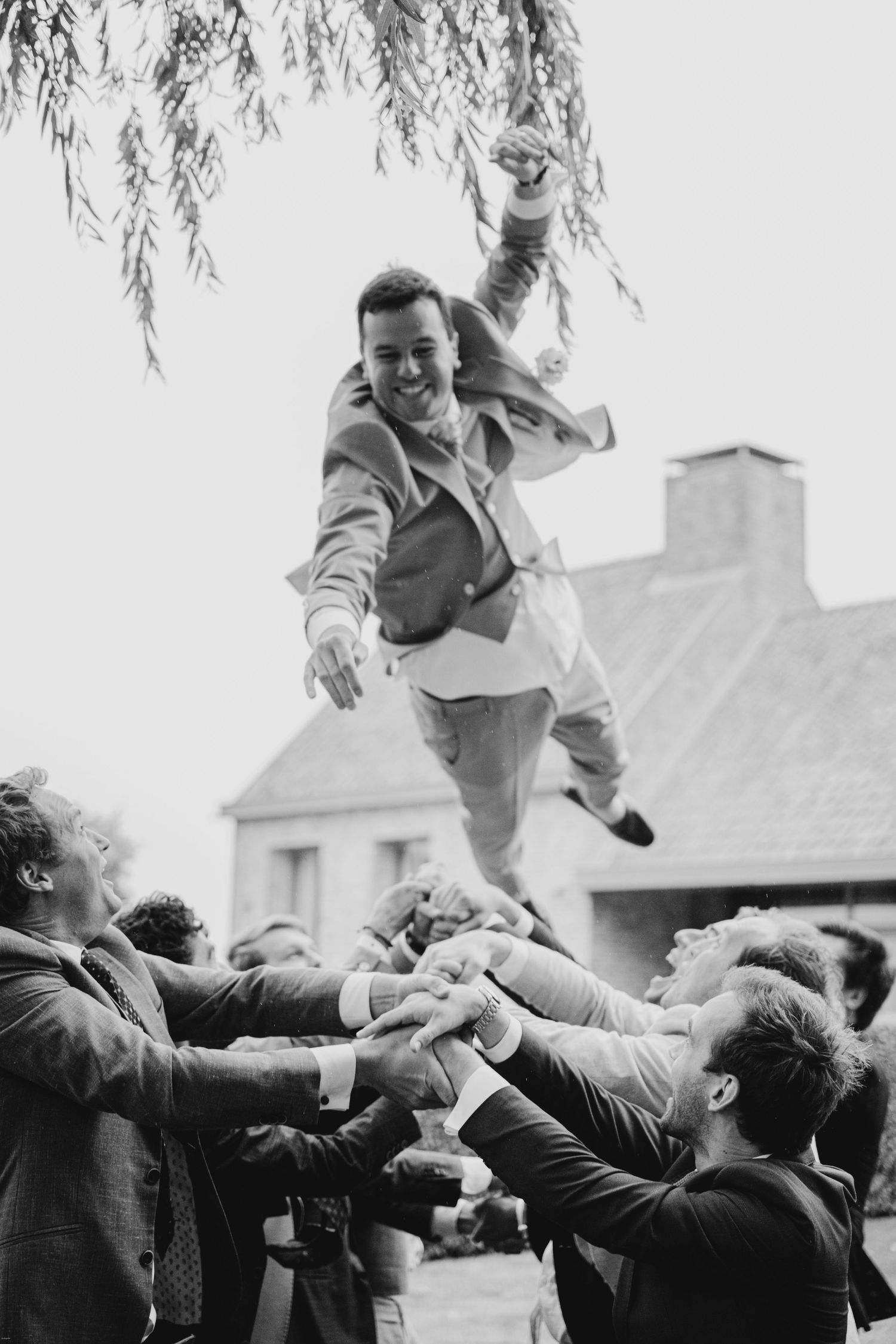 Black and white photo showing celebratory group toss at outdoor wedding.