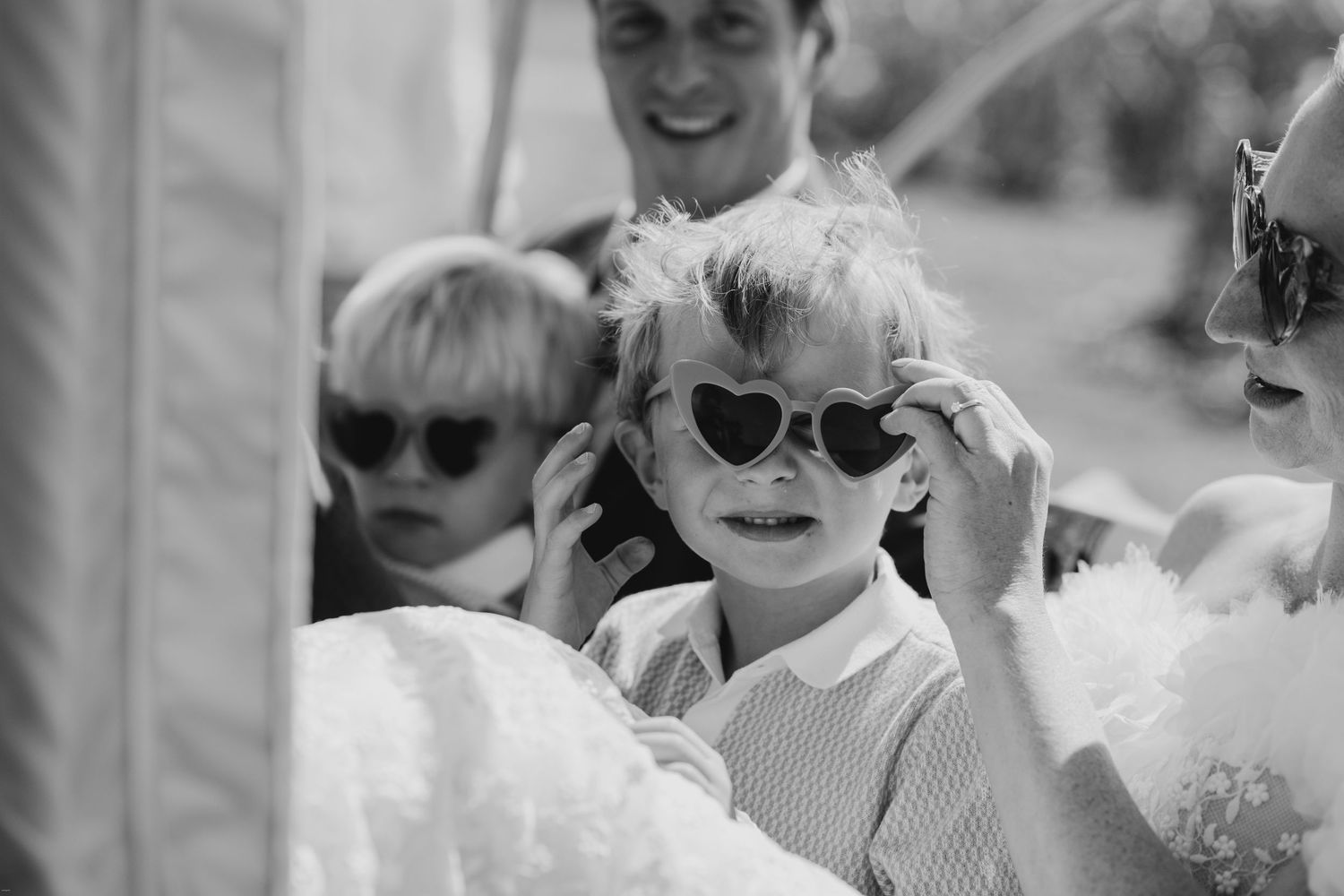 Wedding guests enjoy a sunny outdoor celebration wearing heart-shaped sunglasses.