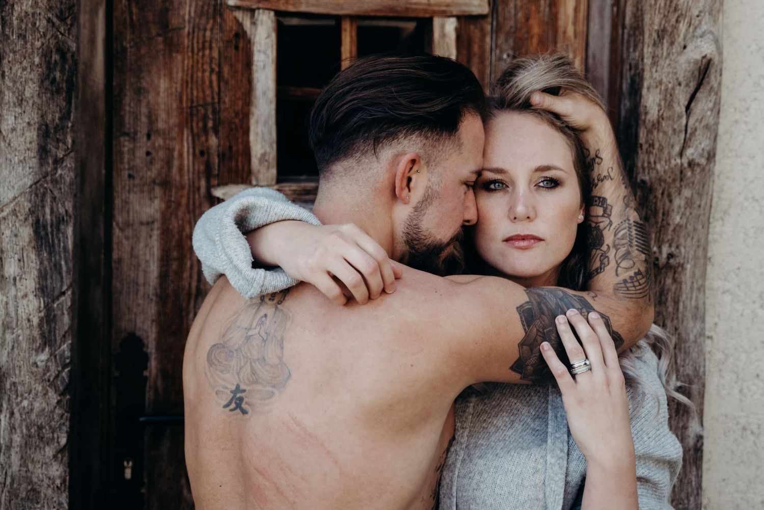 A romantic couple embraces against a rustic wooden wall backdrop in an intimate photoshoot.