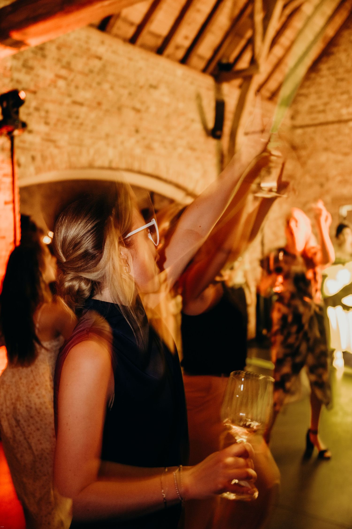 Wedding guests mingling and dancing at a dimly lit reception venue with brick walls.