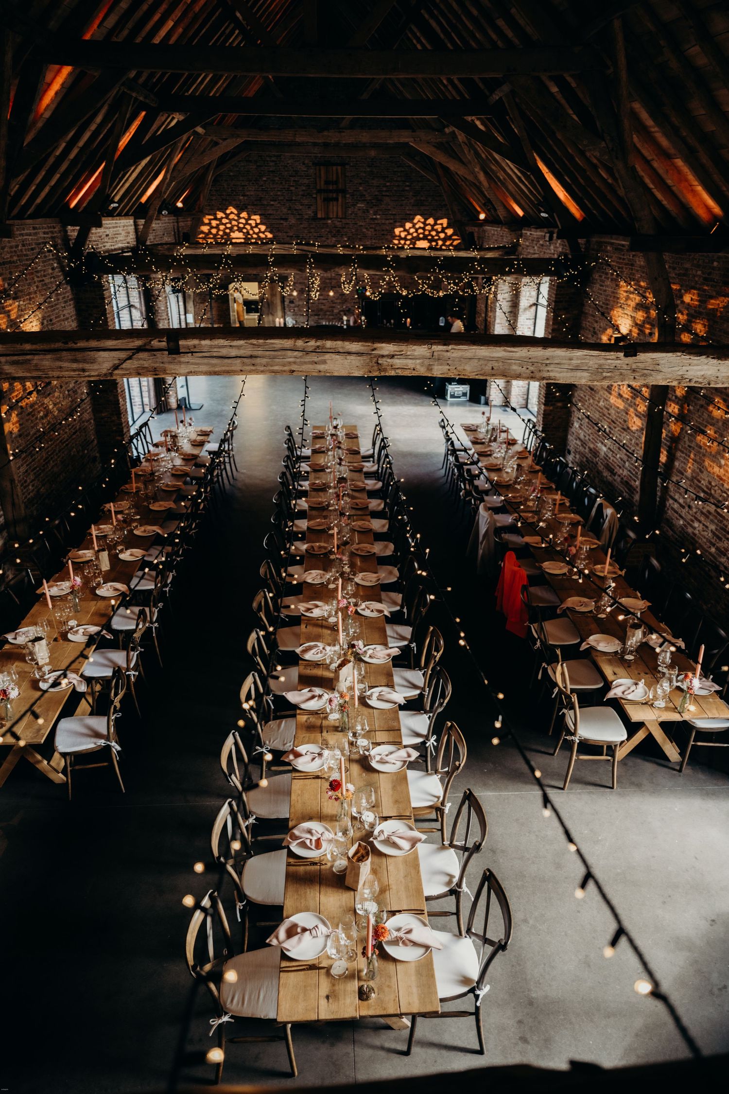 Elegant barn reception setup with long wooden tables and ambient lighting.
