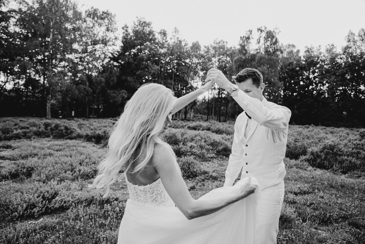Couple dancing and twirling in an outdoor field during sunset.