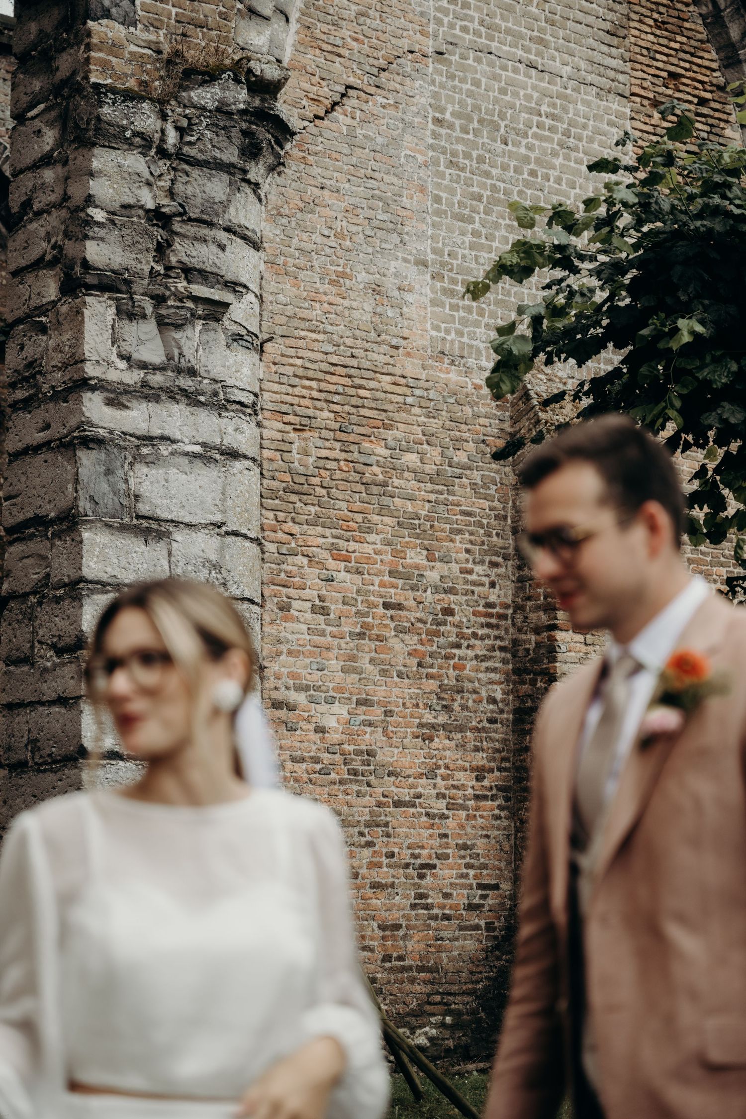 Artistic wedding portrait against brick wall with soft focus and natural lighting.