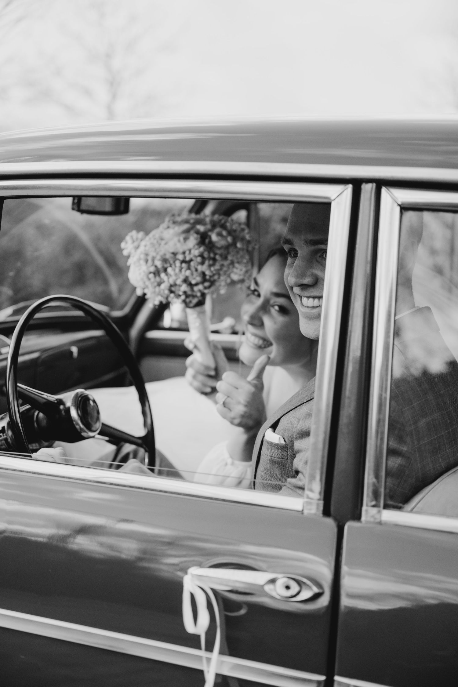 Wedding party riding in a vintage car with retro black and white photography style.