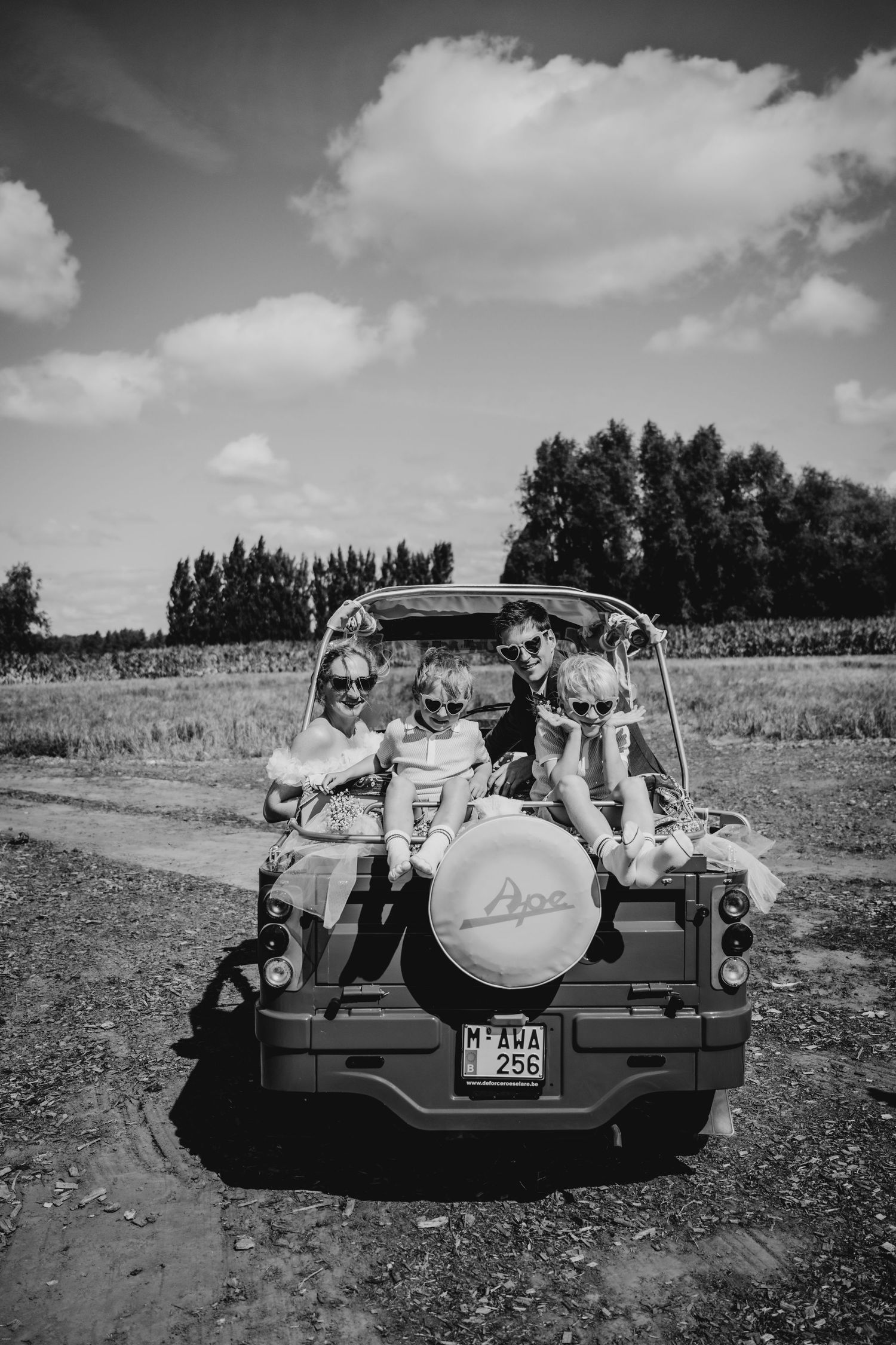 Classic car carrying wedding party along countryside road in black and white.