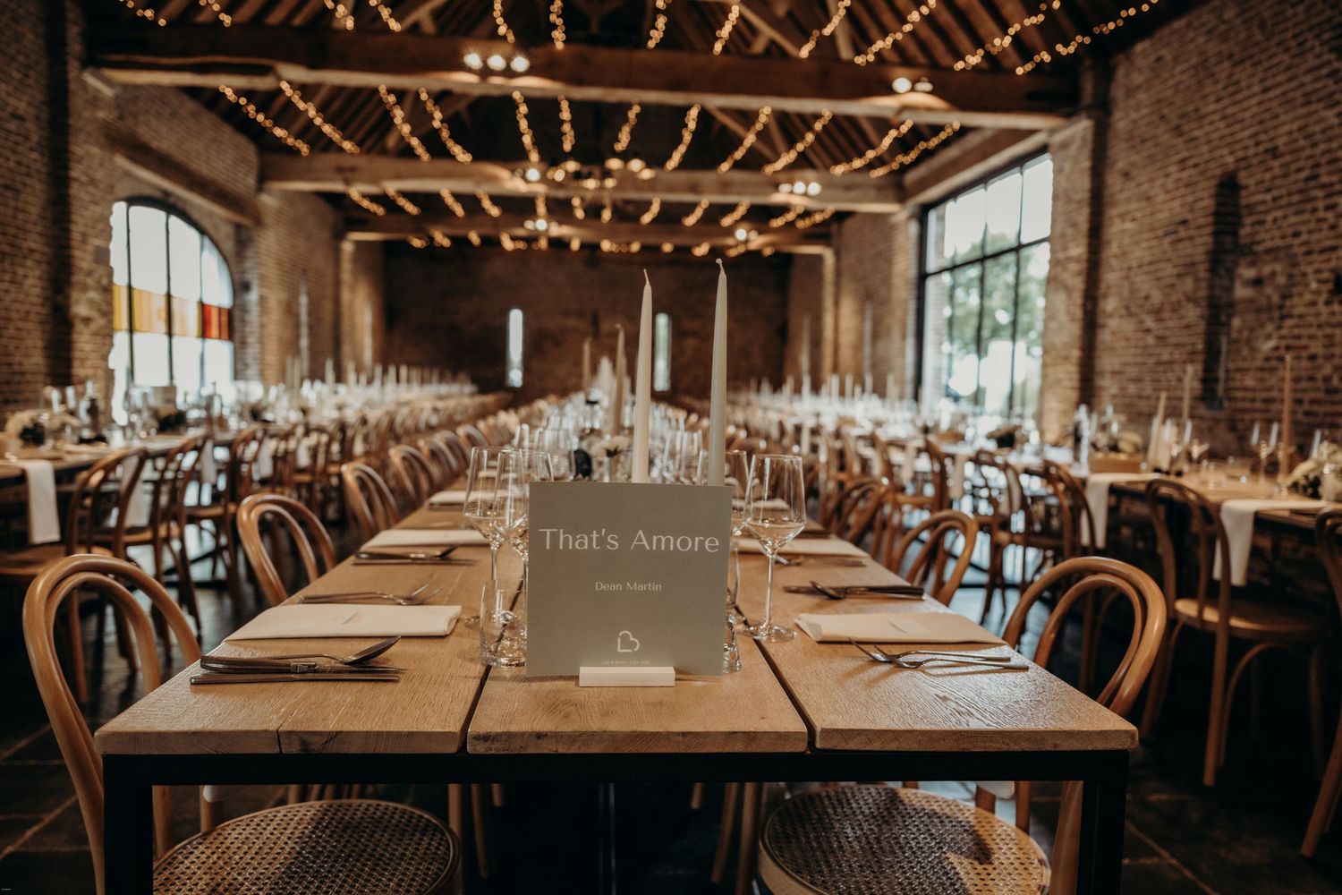 Wedding reception venue with long wooden tables and string lights hanging from industrial ceiling.