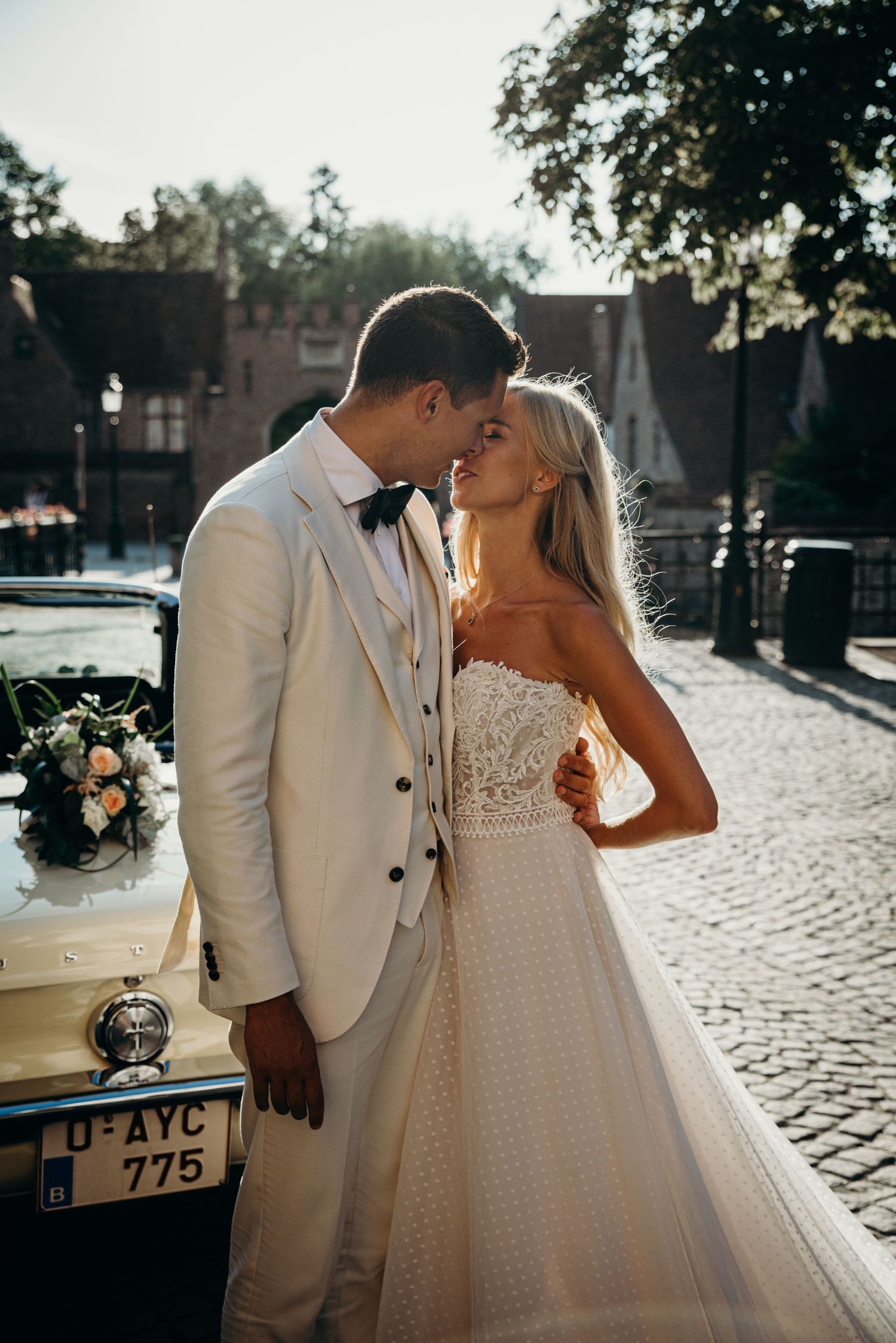 Romantic moment between newlyweds in elegant white attire on cobblestone street.