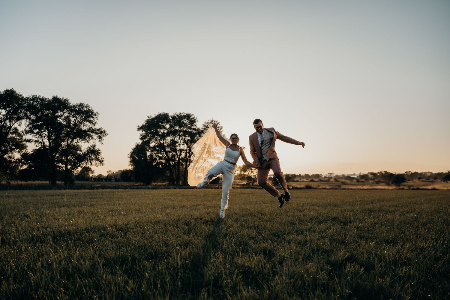 Panoramic sunset view of couple in open field with trees in background.