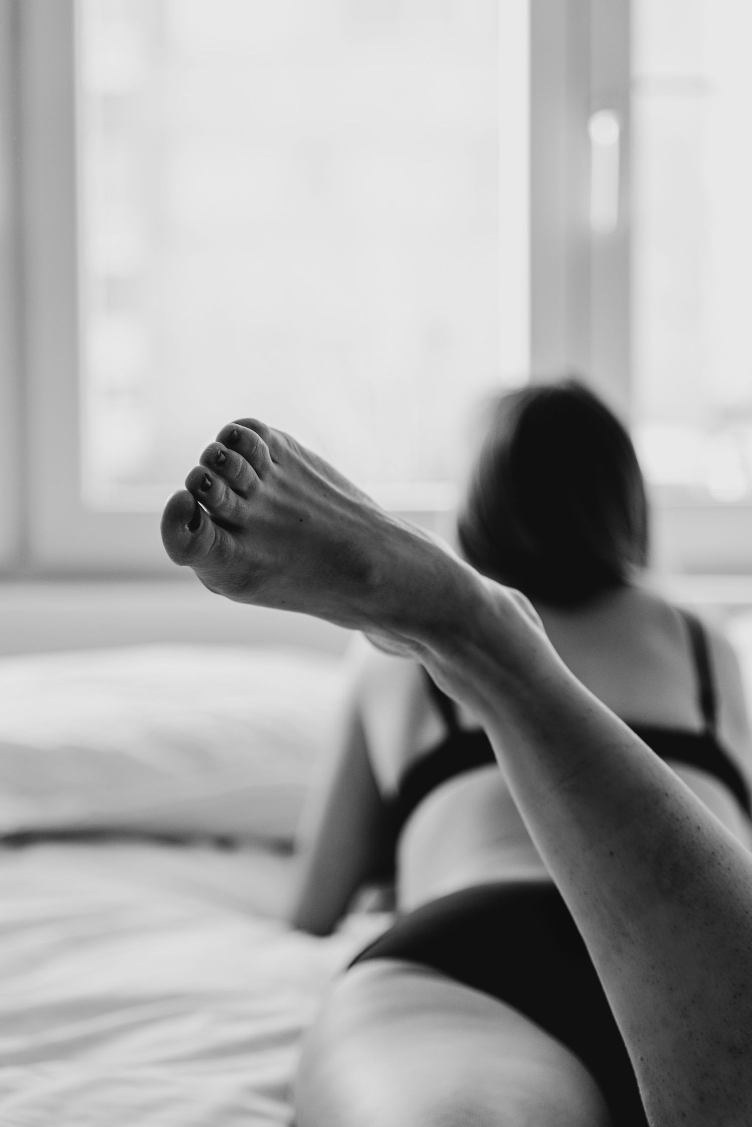 Black and white artistic photograph showing bare feet resting on white bedding with a soft, dreamy atmosphere.