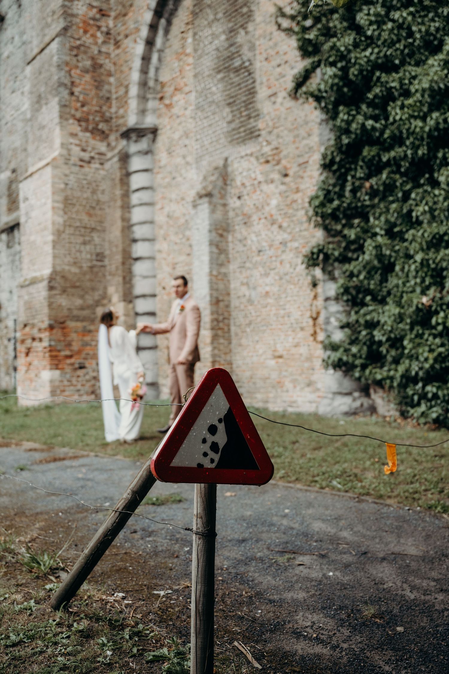 Wedding couple walking along historic brick wall with metal barrier in foreground.