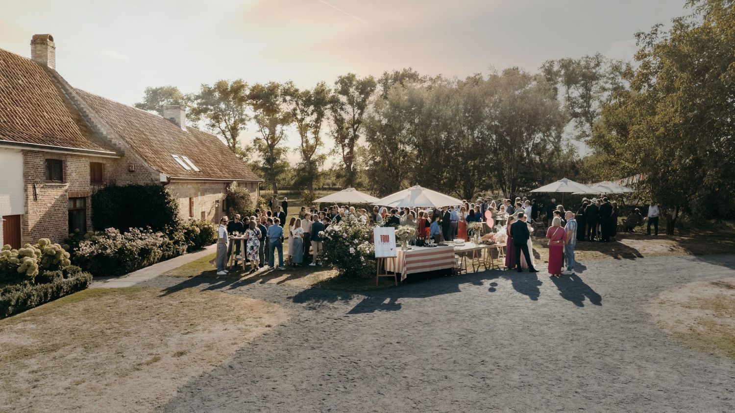 Panoramic view of a rustic wedding venue with guests gathered at sunset.