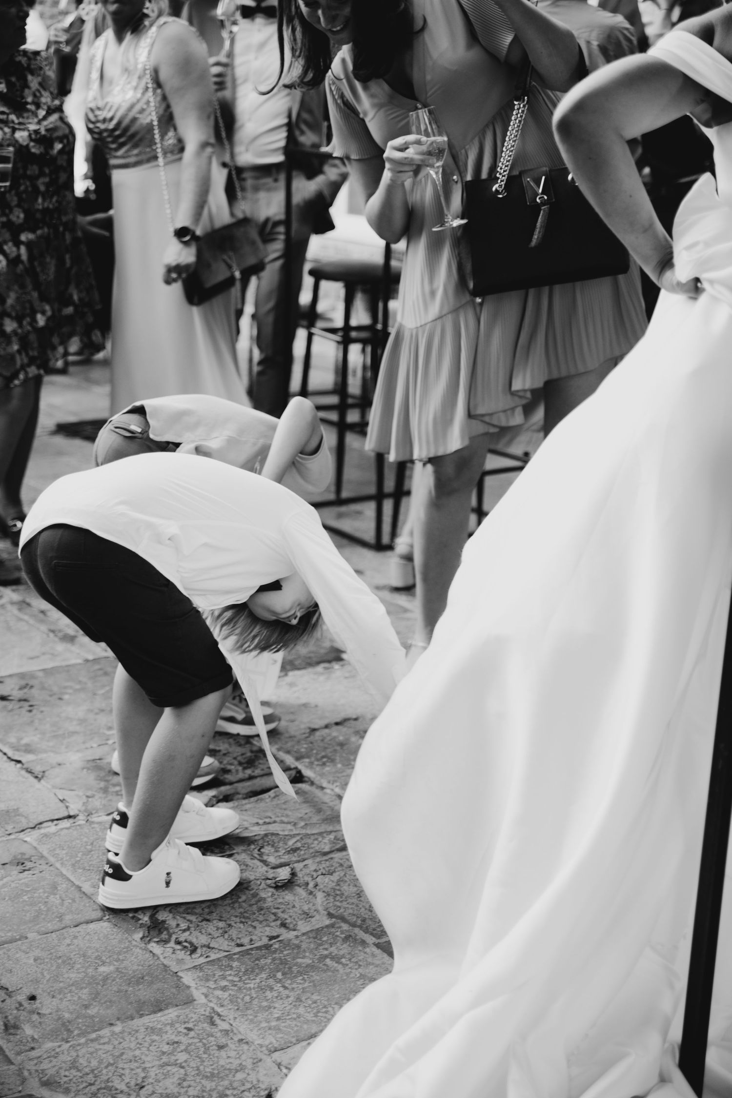Black and white photo of someone adjusting a wedding dress train outdoors.