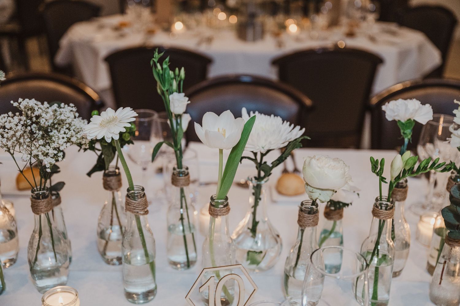 Elegant wedding reception table decorated with simple floral arrangements in glass vases.