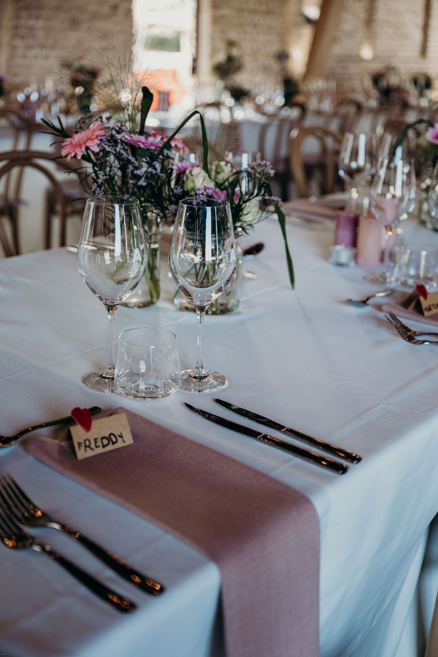 Wedding reception table with pink runner, floral centerpieces and elegant place settings.