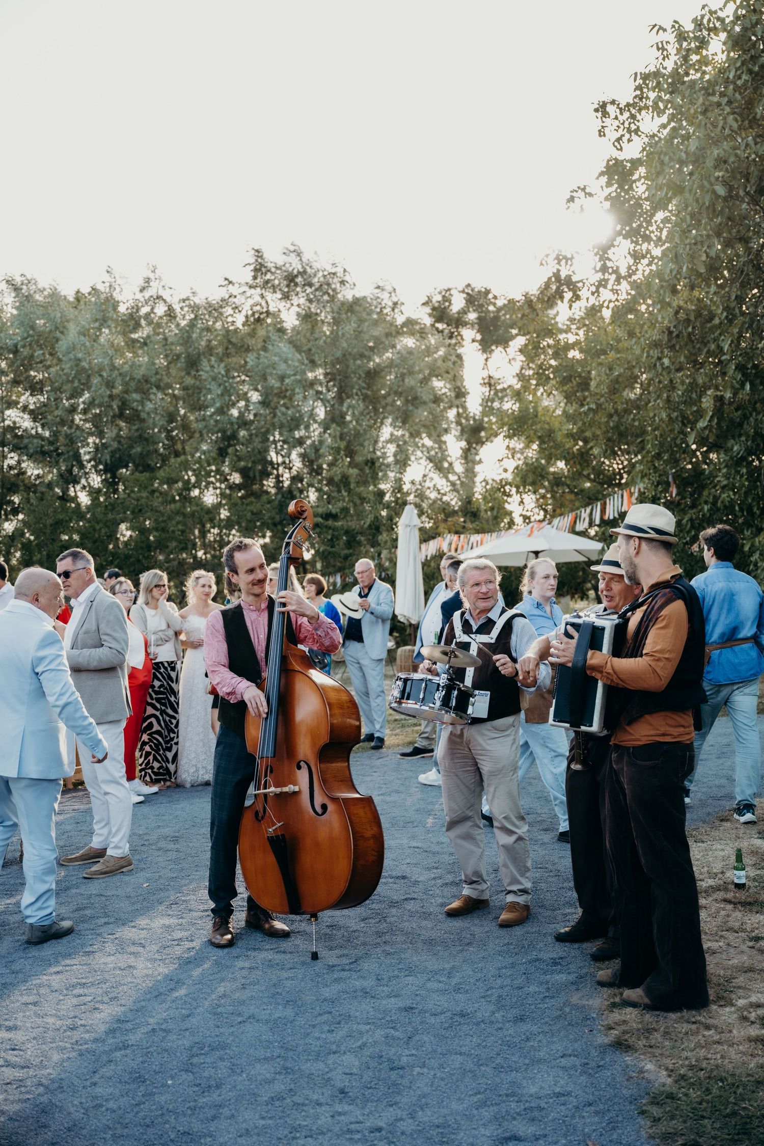 Musicians with upright bass perform at an outdoor gathering with guests mingling.