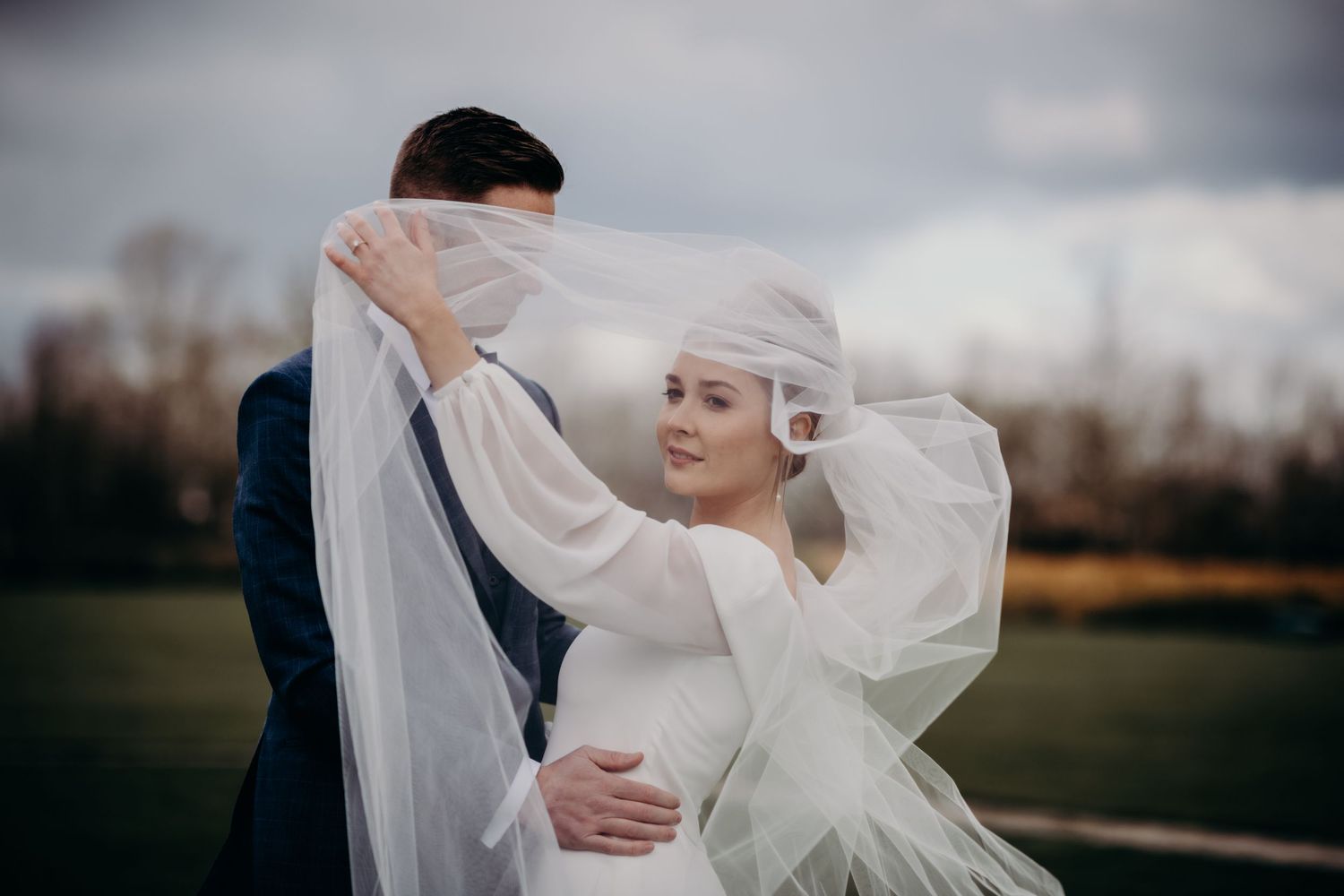 Romantic wedding photoshoot with billowing veil in natural outdoor setting.
