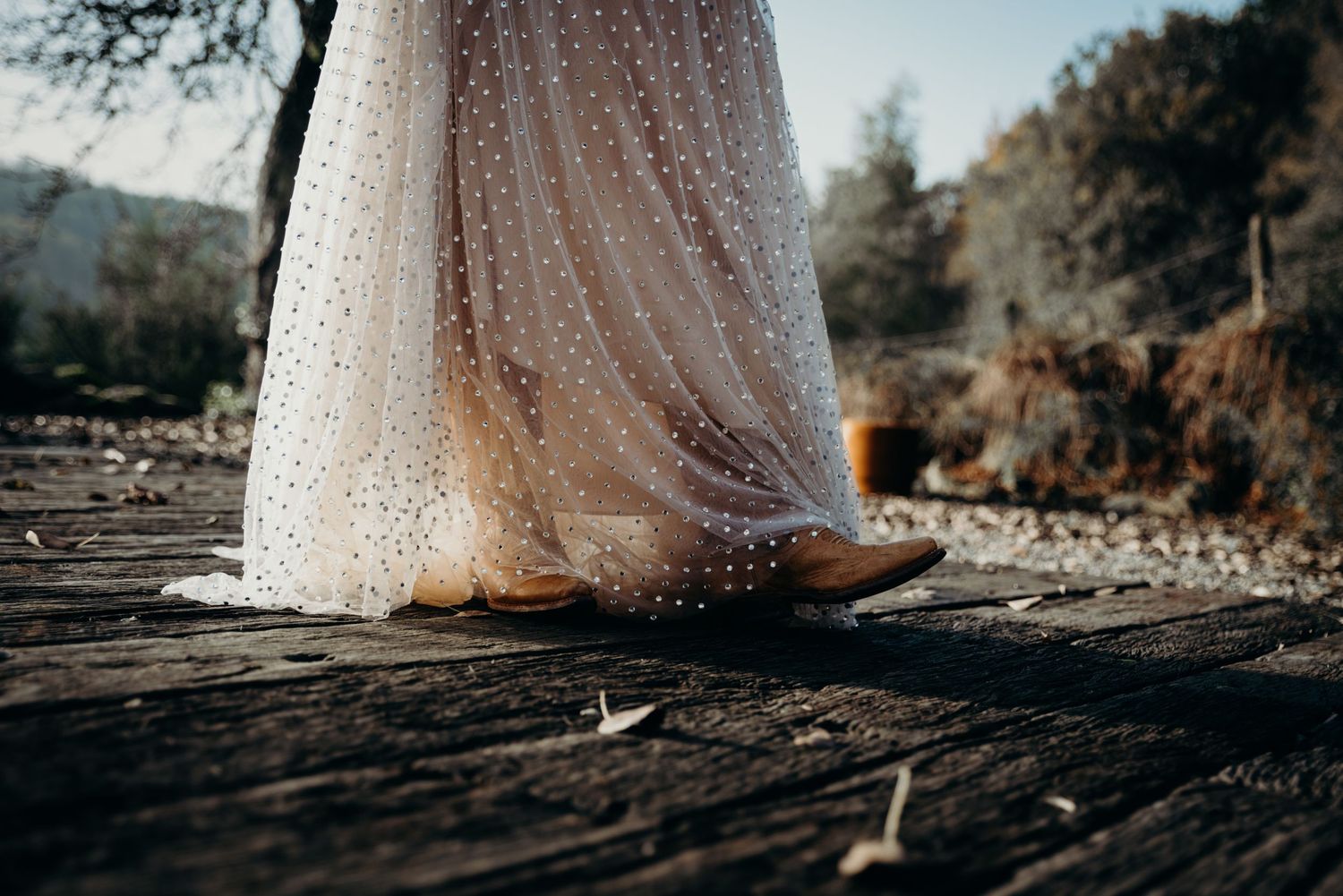 Close-up detail of lace wedding dress hem on wooden deck.