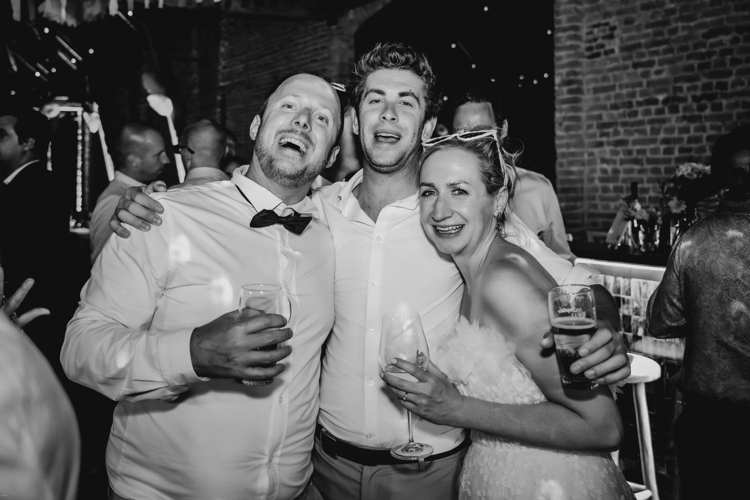 Friends celebrate together at a wedding reception with drinks in hand.