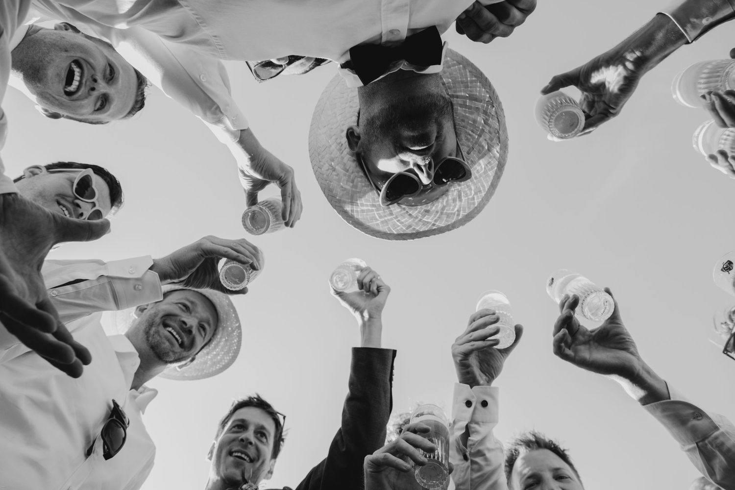 Low angle view of people raising drinks in a celebratory toast against a bright sky.