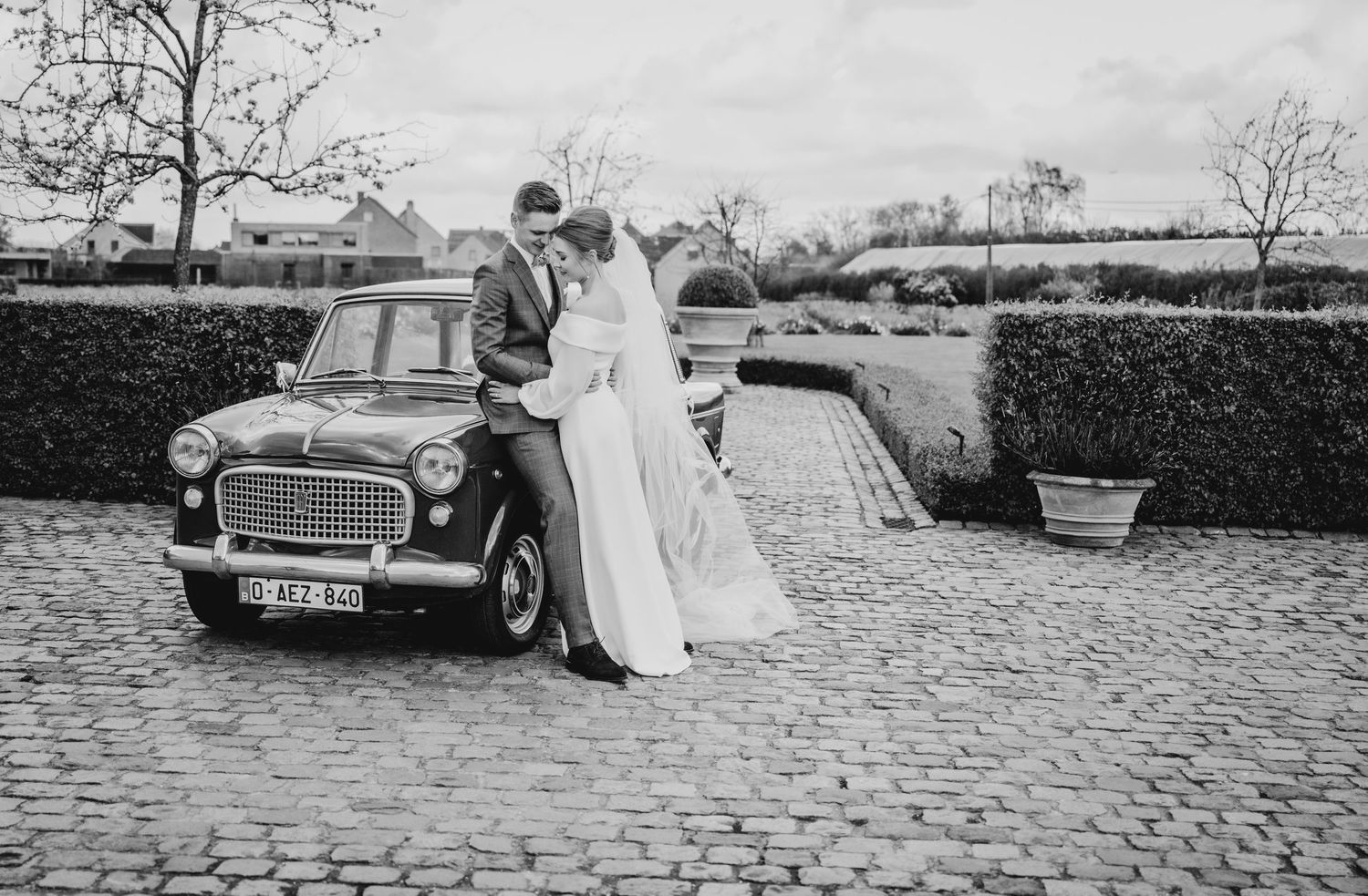 Vintage car parked on cobblestone driveway during a wedding celebration.