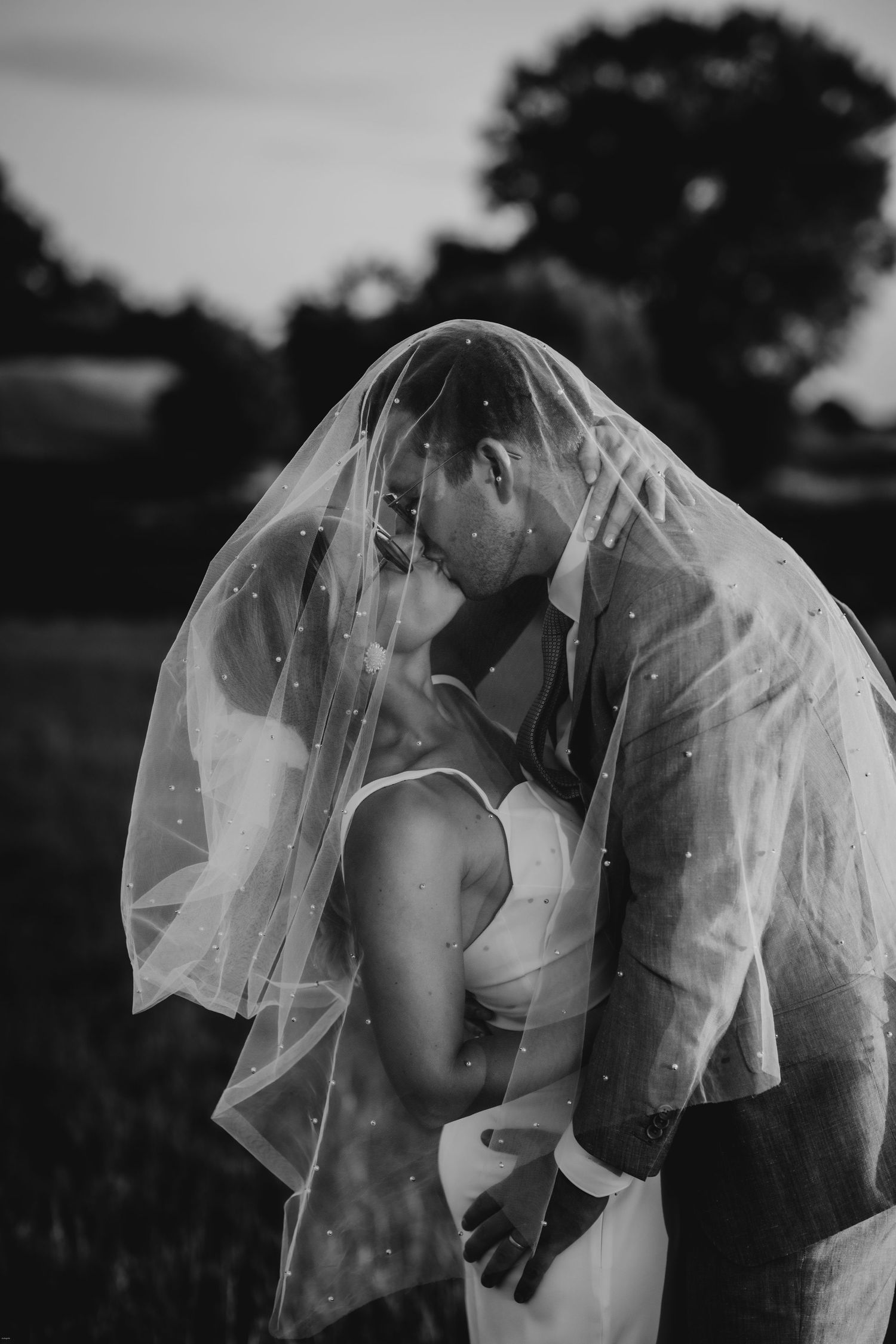 Romantic black and white photo of a couple in wedding attire with flowing veil.