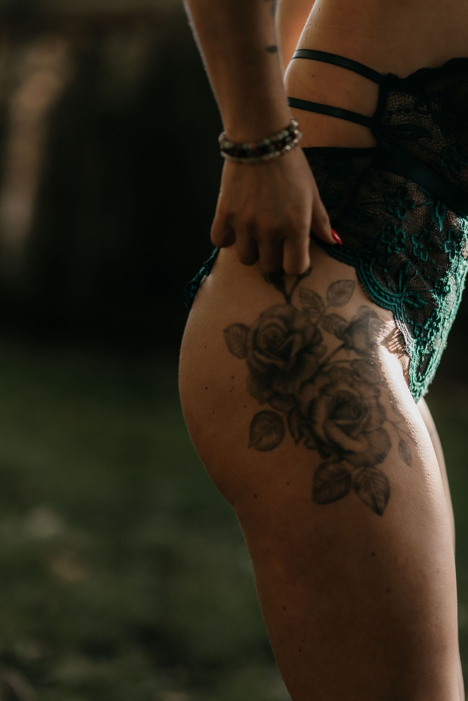 Close-up view of a floral rose tattoo design on skin in dark moody lighting.
