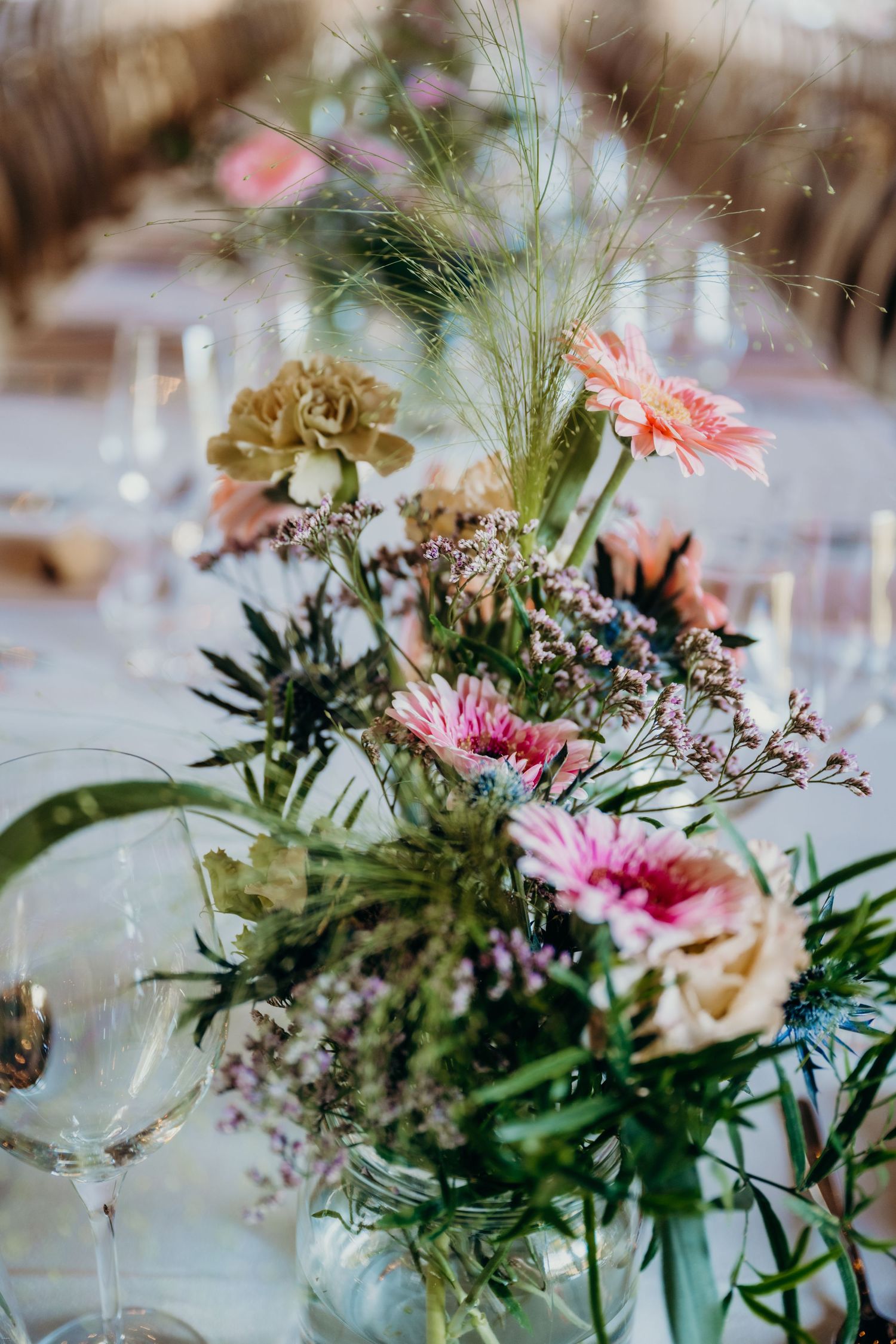 Delicate floral centerpieces with pink gerbera daisies and greenery in glass vases.