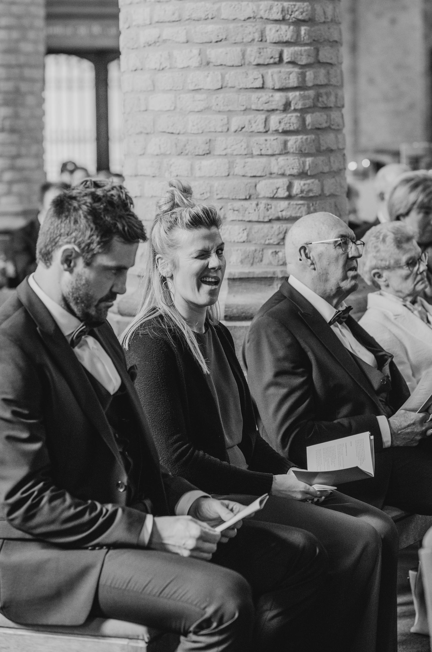Guests seated in formal attire at a church ceremony read from programs during a wedding service.