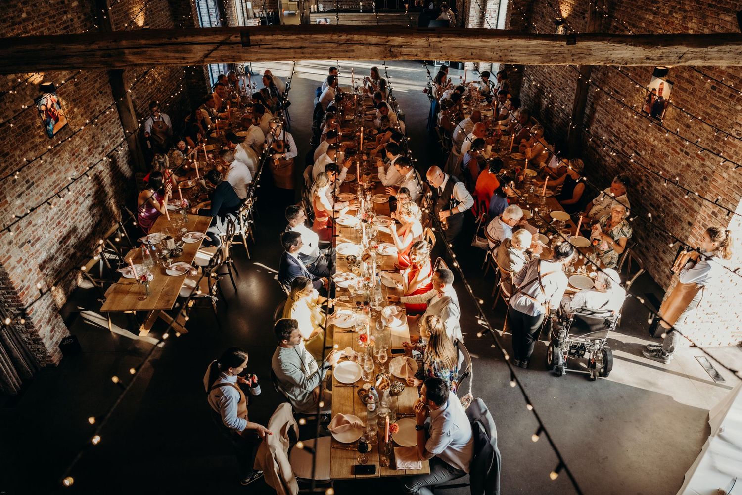 Wedding reception guests seated at rustic brick-walled venue with warm lighting and elegant table settings.