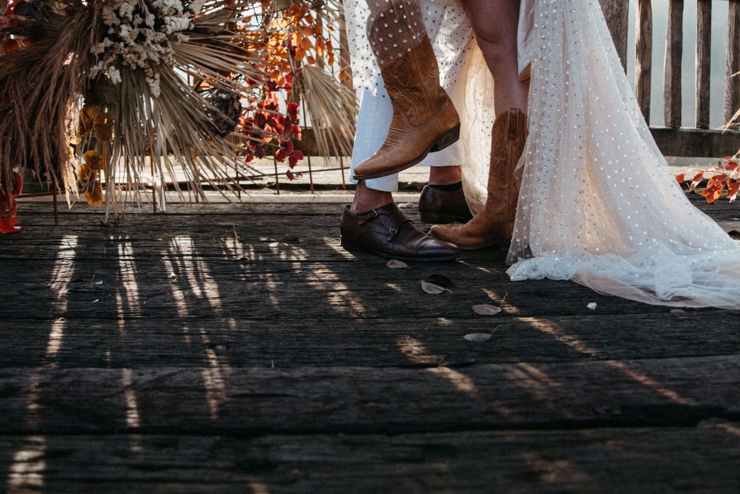 Wedding couple embraces on wooden deck with dramatic lighting and shadows.
