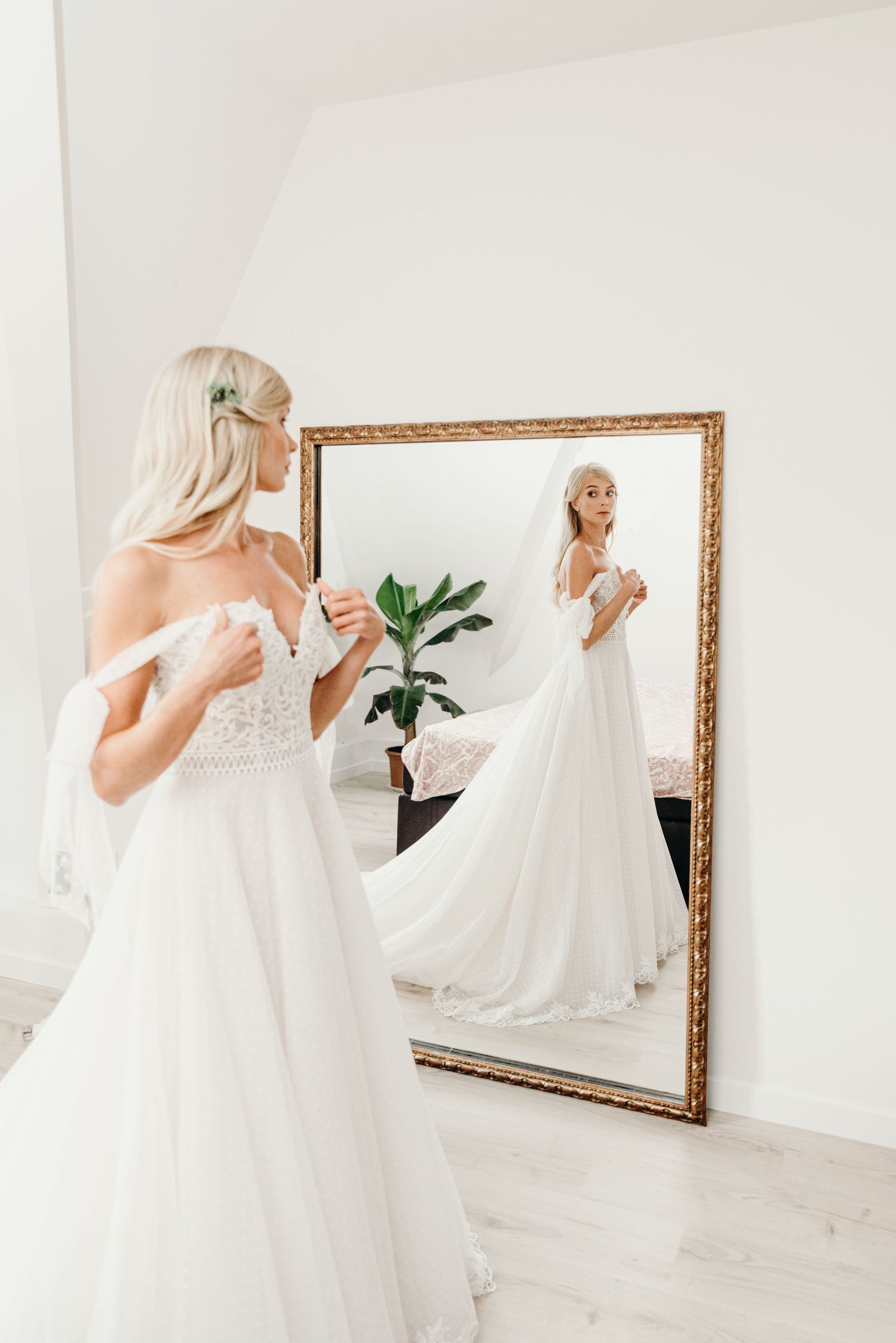 Bride admiring her wedding dress reflection in a large gold-framed mirror.