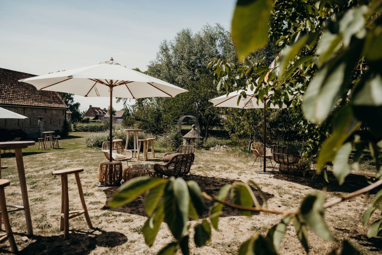 Outdoor wedding venue setup with white umbrellas and rustic wooden furniture in a garden setting.
