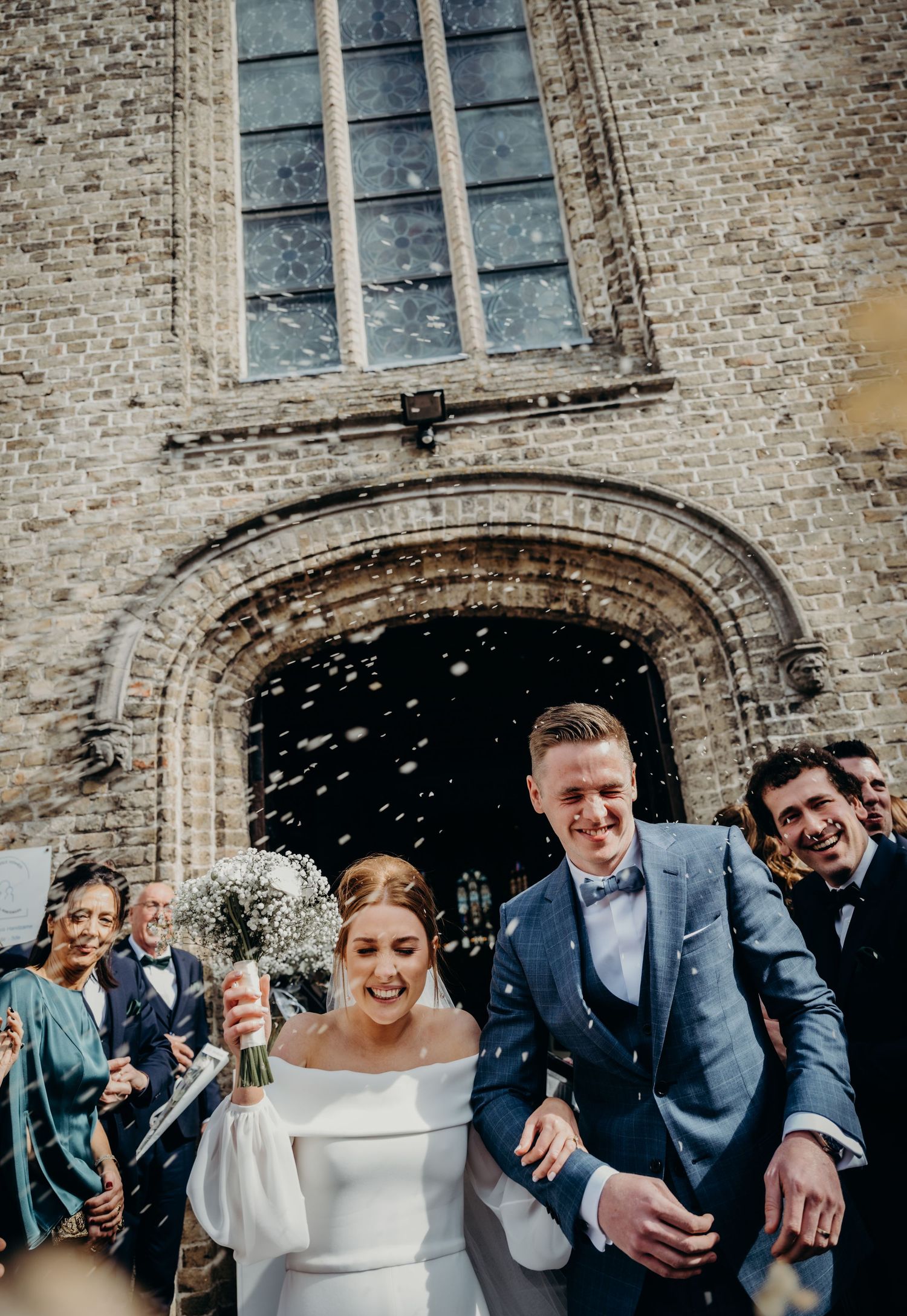 Wedding party celebrating with confetti outside a historic brick church building.