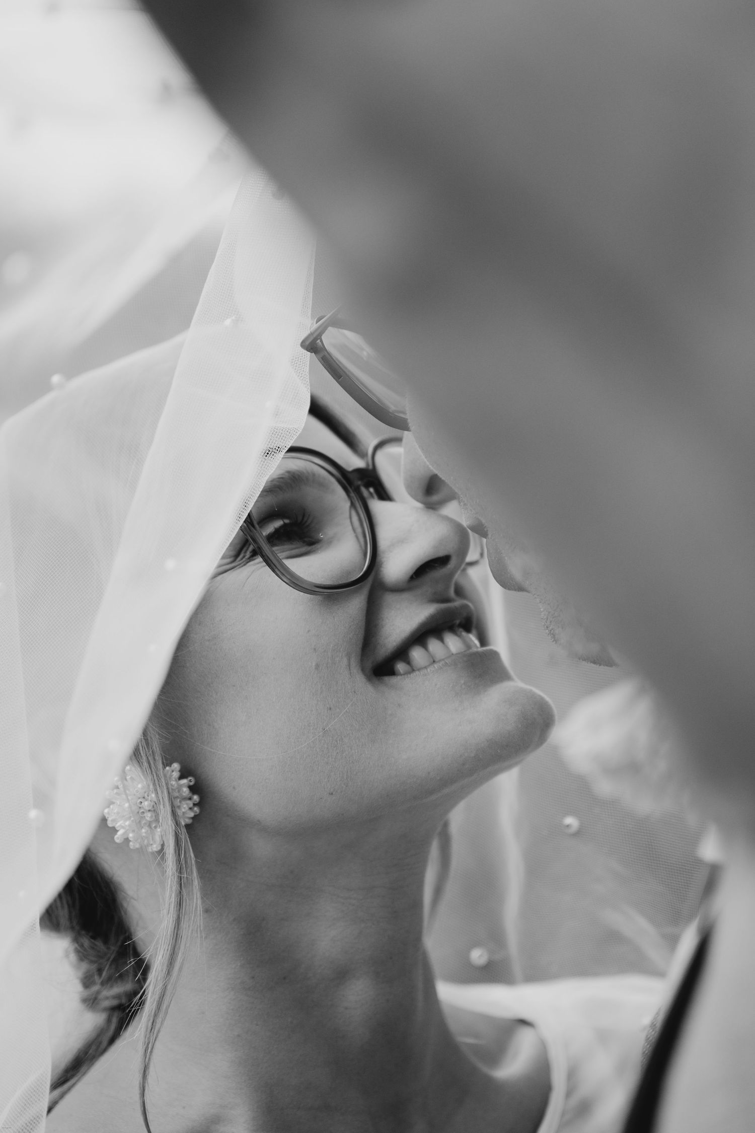 Close-up black and white portrait showing joyful expressions through a delicate white veil.